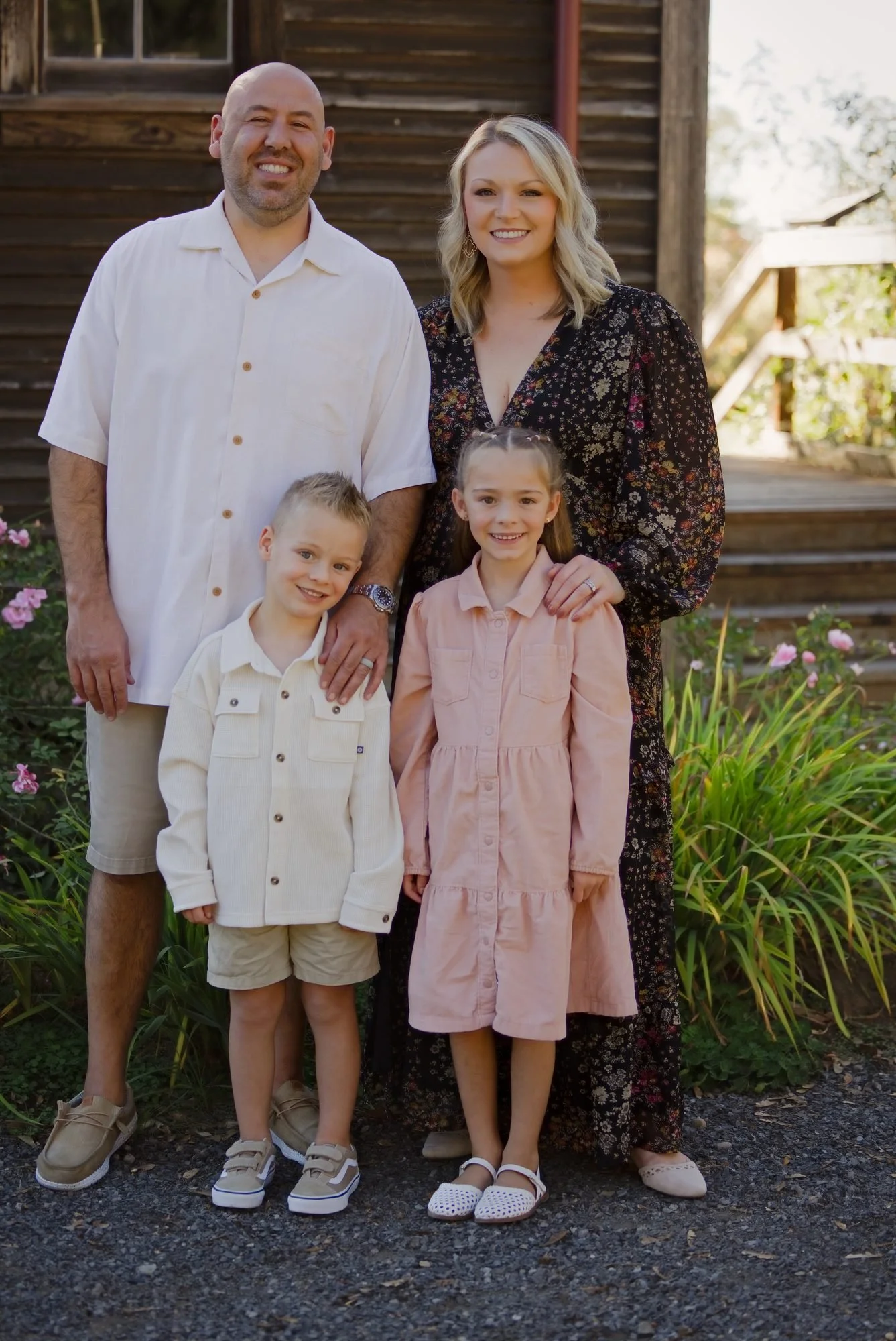 Family of four in cream and blush beside a weathered farmhouse during a fall mini session near Sandy Oregon