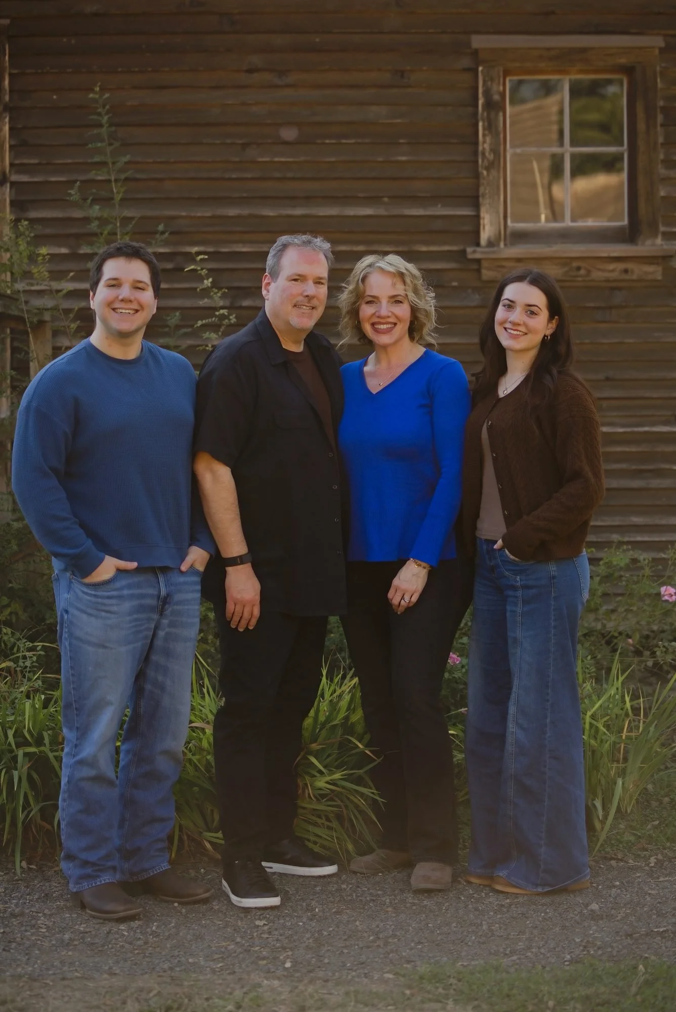 Family of four in navy and blue in front of a weathered wood barn wall on a farm in Eagle Creek