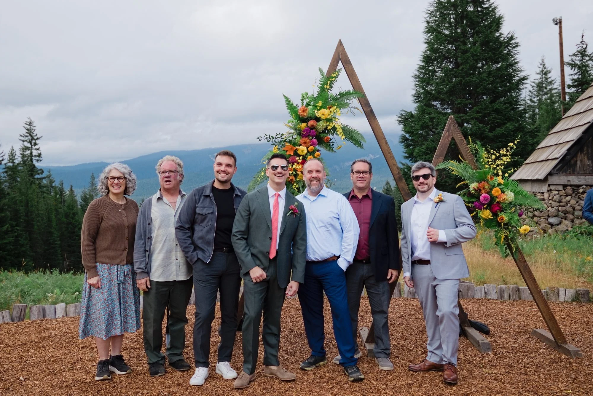 The grooms with their wedding party in front of the wooden triangle arch at Skibowl