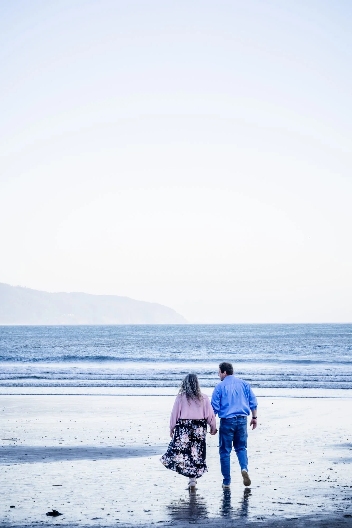 Tori and Jamie walking hand in hand along the surf at Cape Kiwanda