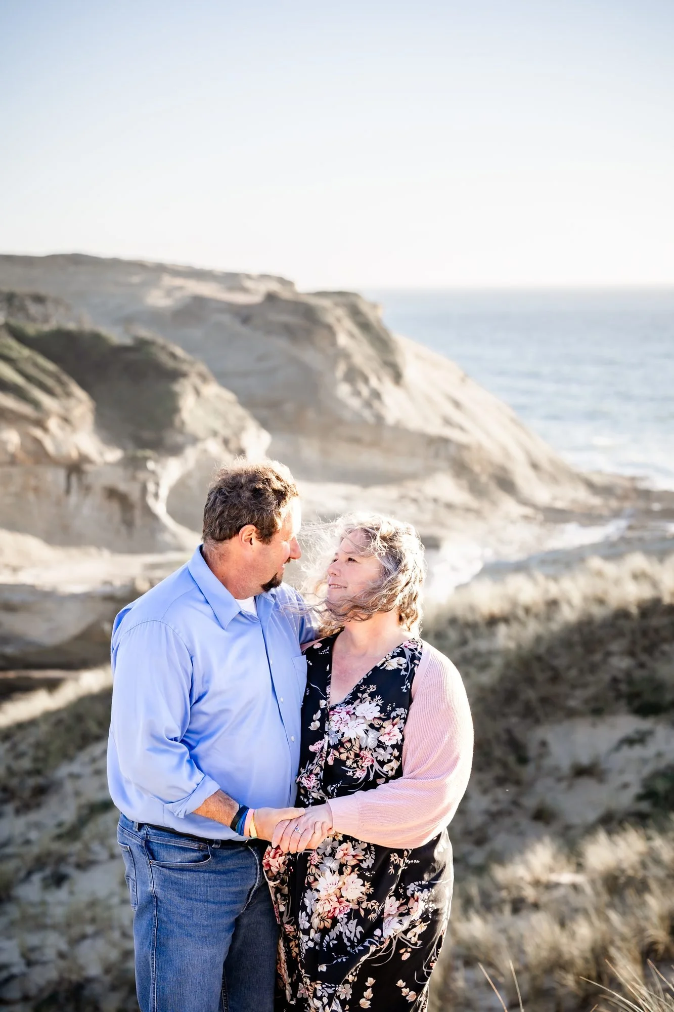 The couple holding each other beneath the sandstone cliffs at Cape Kiwanda, Pacific City Oregon engagement photographer