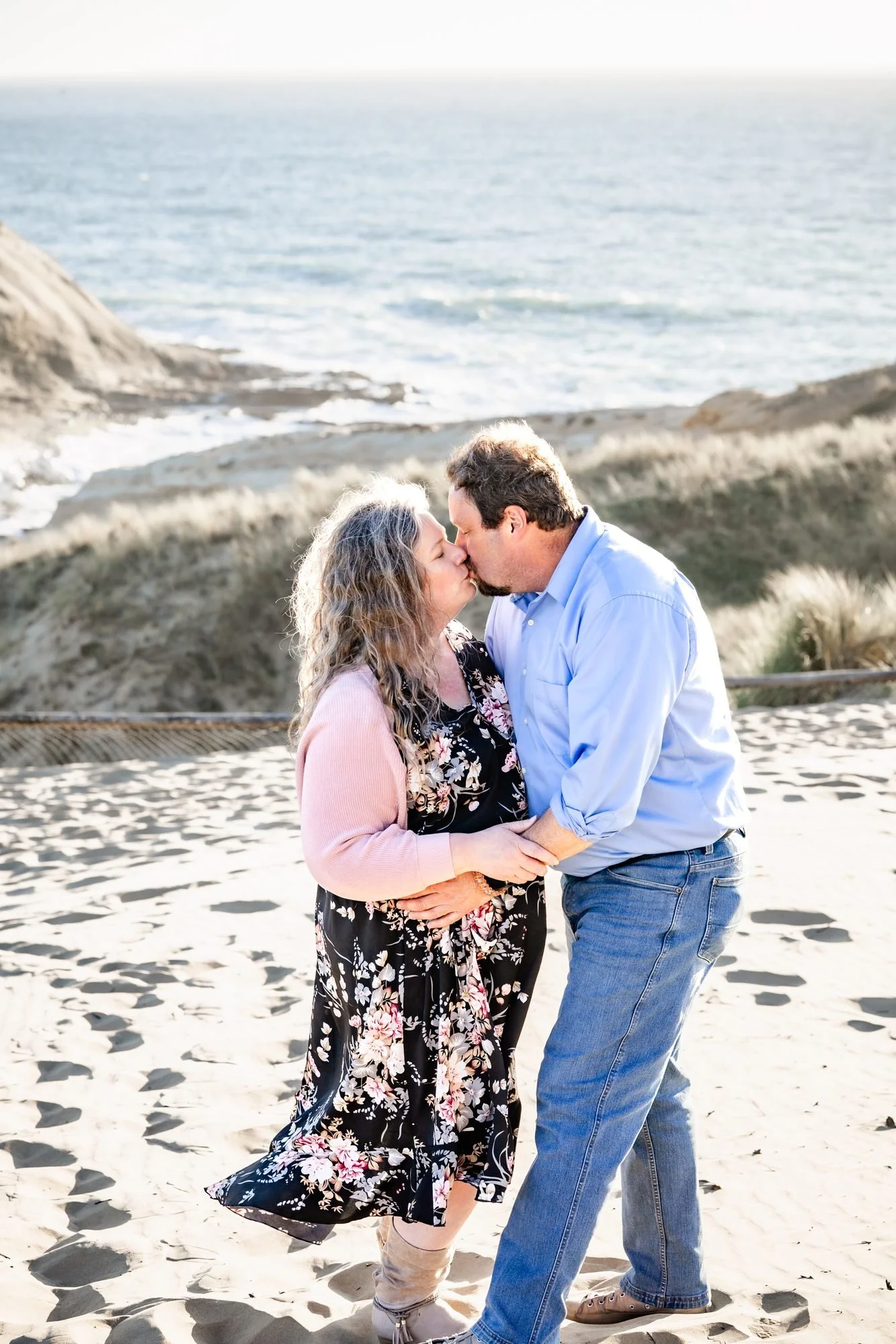 The couple kissing on the beach with footprints in the sand at Cape Kiwanda
