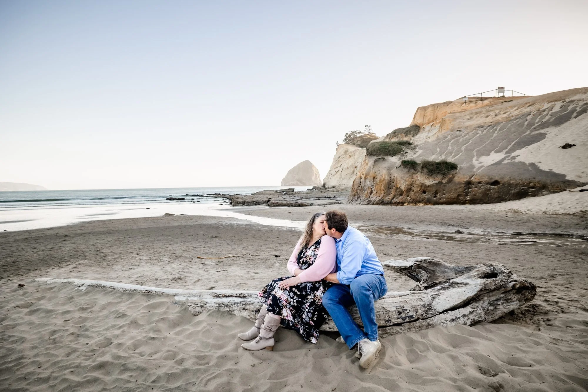 Tori and Jamie sitting on driftwood beneath the cliffs at Cape Kiwanda