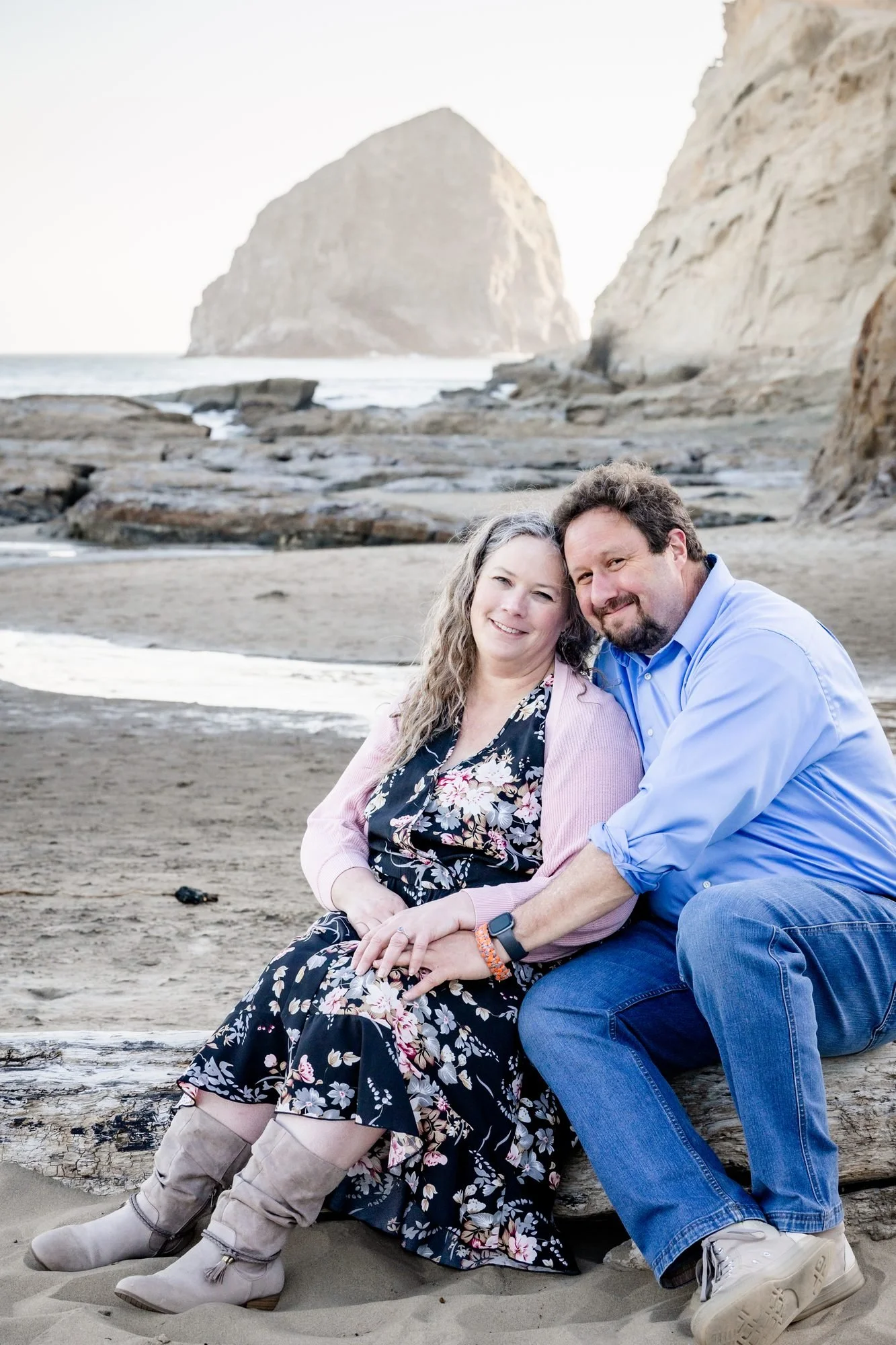 Tori and Jamie sitting together on the rocks with Haystack Rock behind them in Pacific City