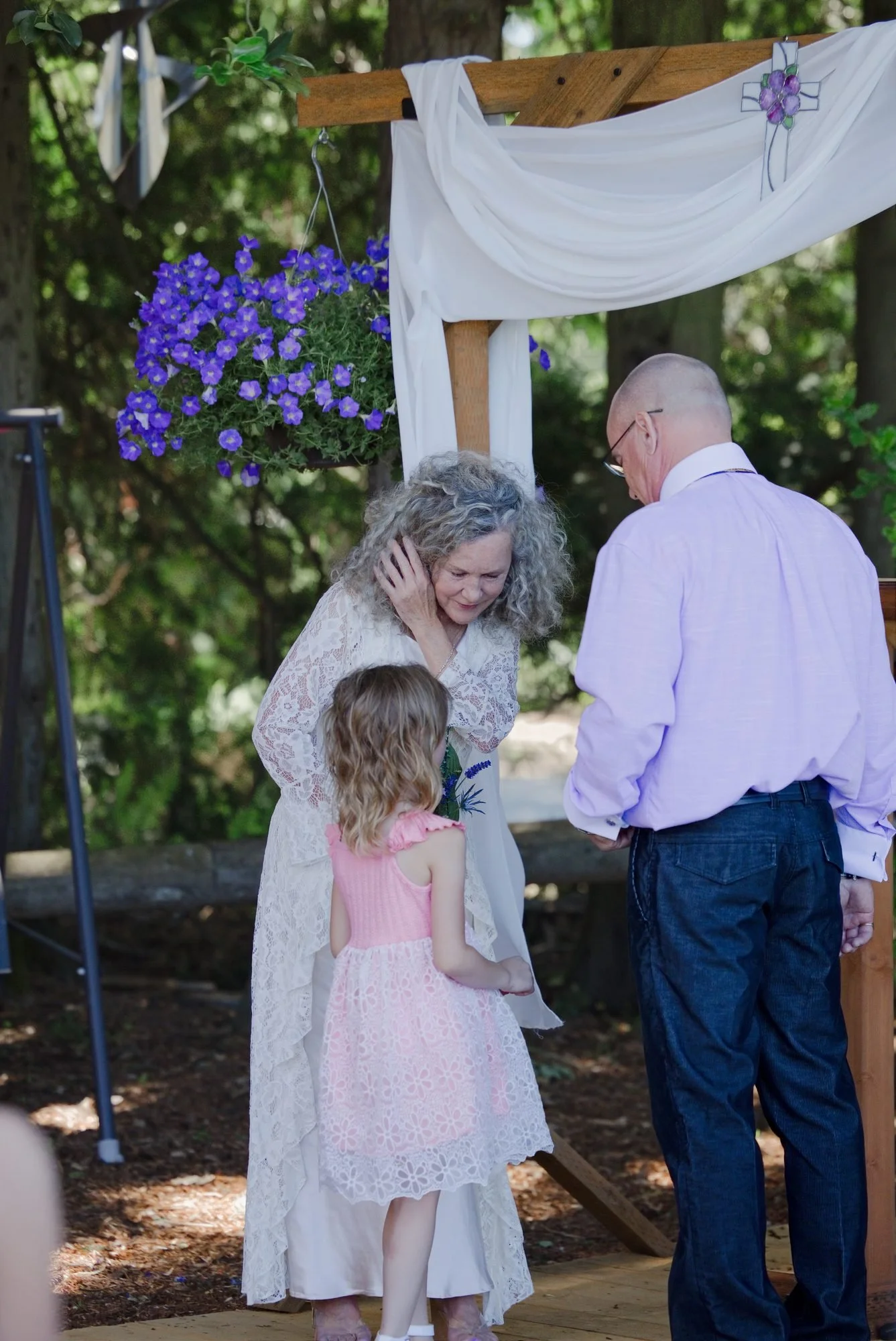 Trudy hugging a little flower girl in pink under the wedding arch