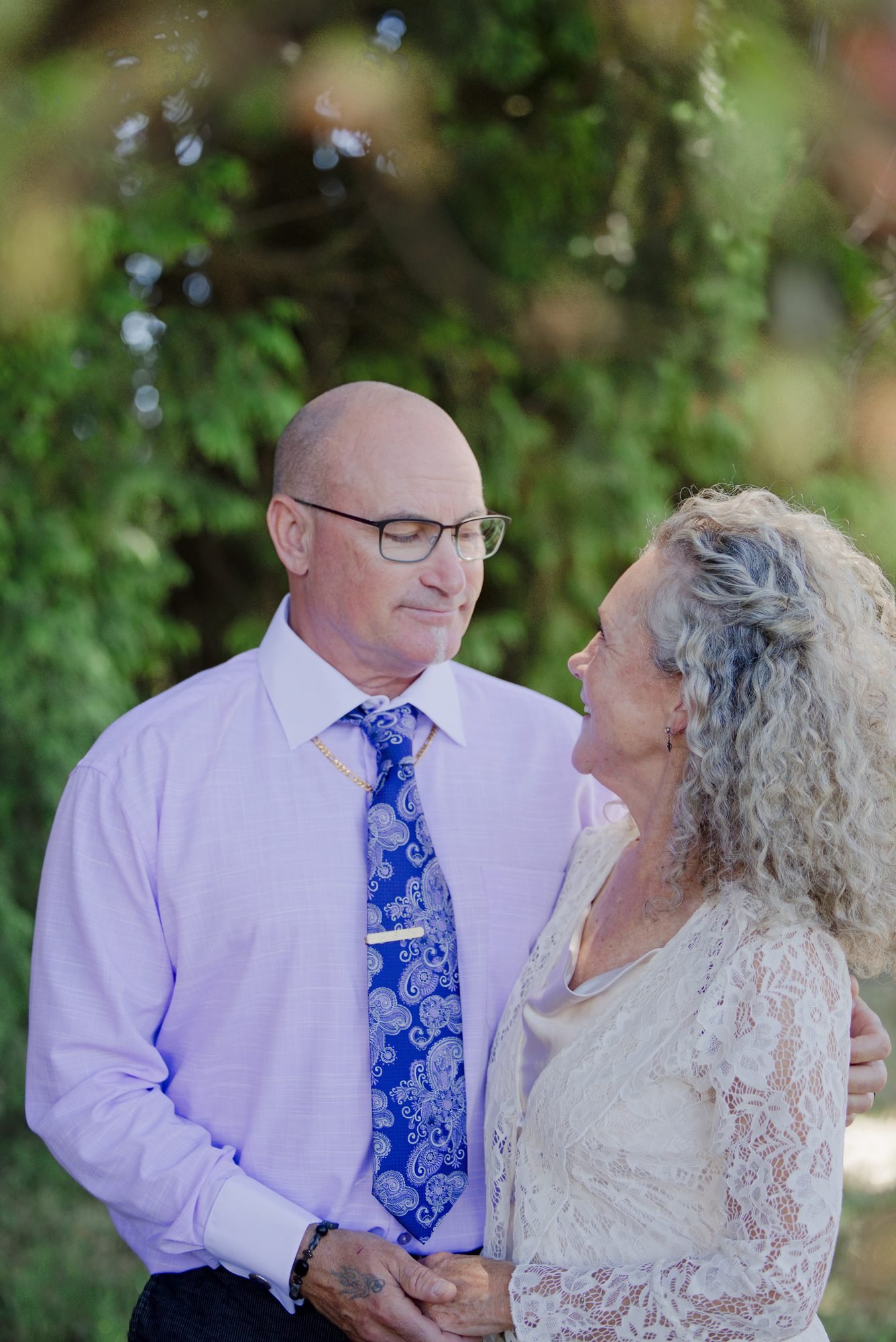 Michael and Trudy looking at each other beneath the pines at their backyard wedding