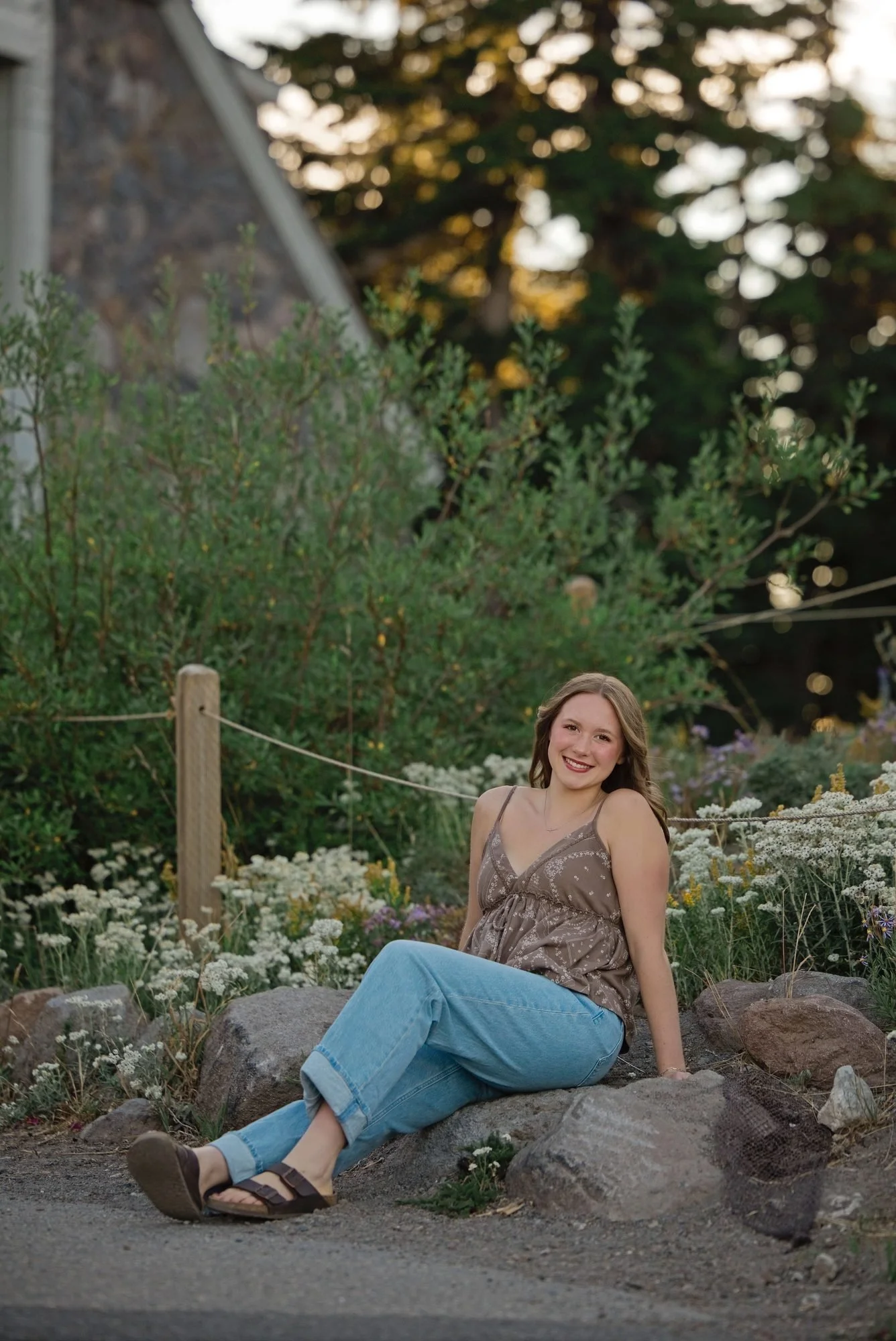This senior sitting among the rocks and wildflowers with the lodge behind her