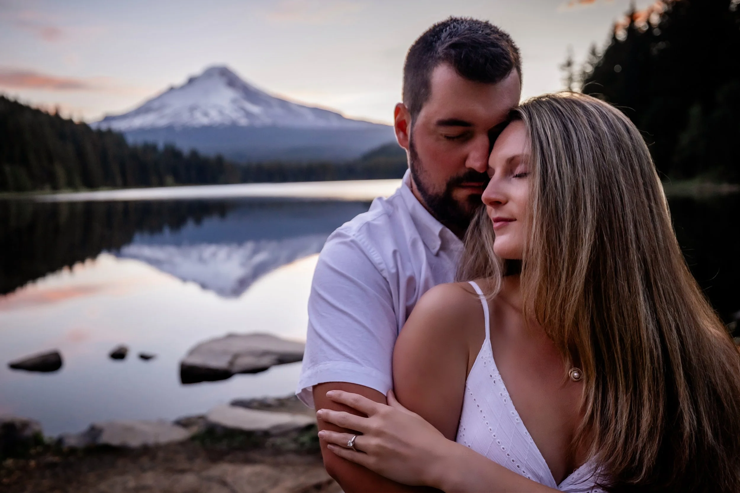 Couple embracing at Trillium Lake at sunset with Mt. Hood reflected in the still water