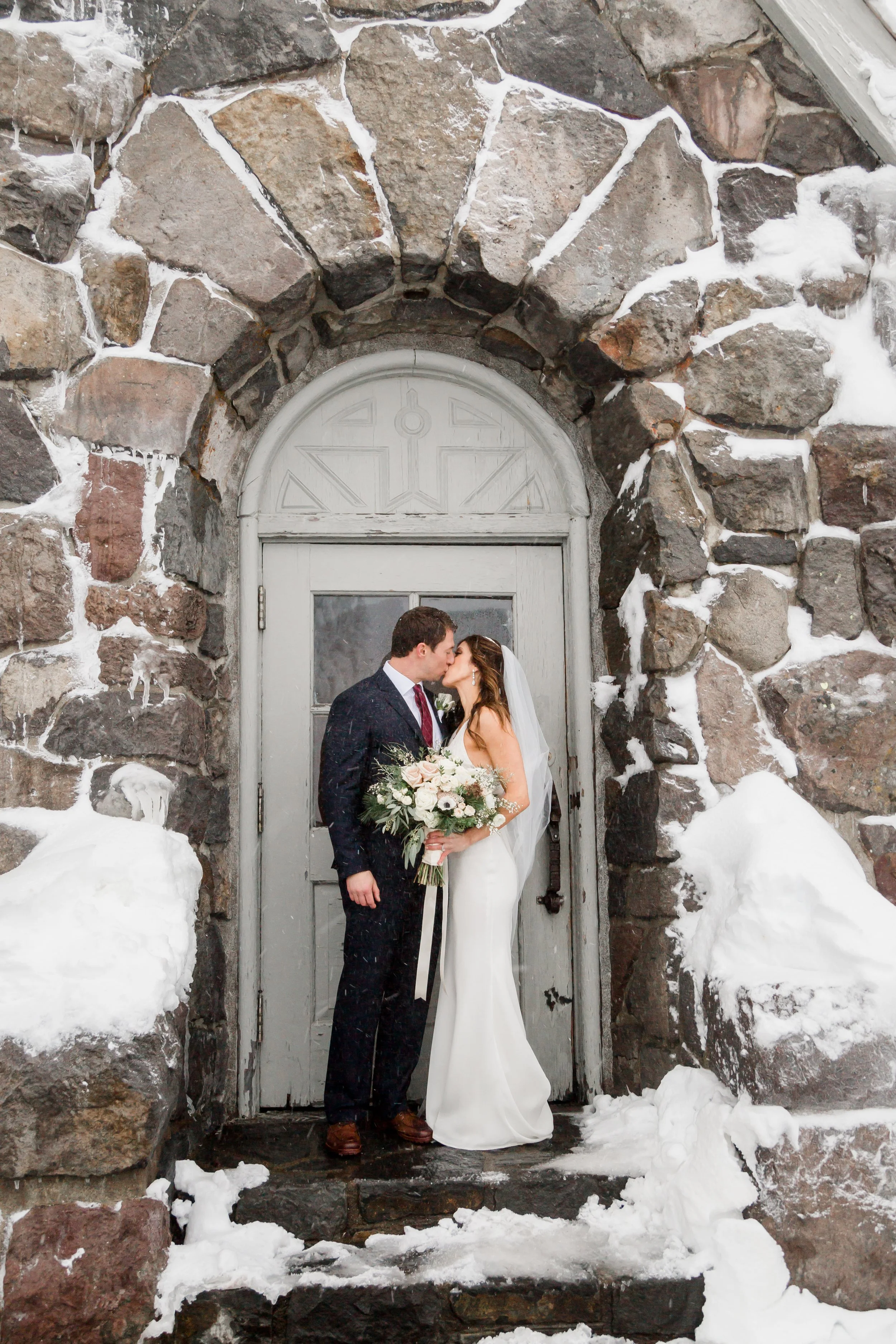 Bride and groom kissing in a snow dusted stone archway at Timberline Lodge on their winter wedding day