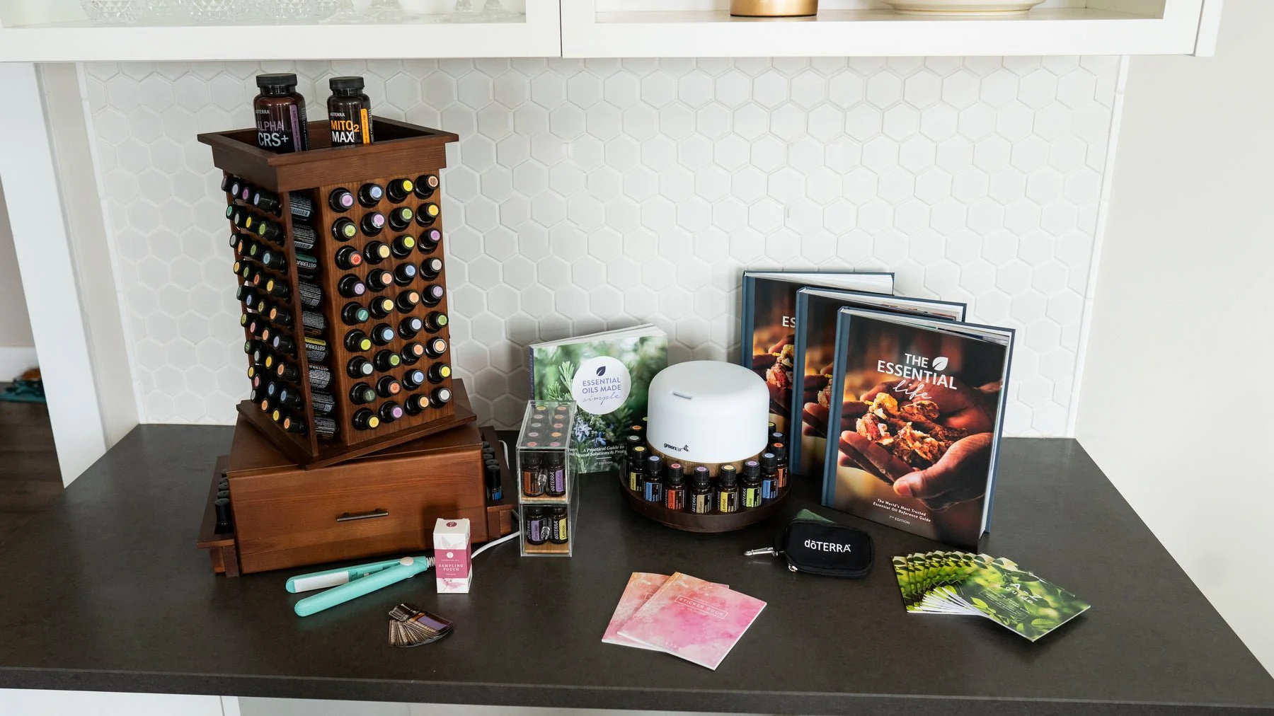Diverse essential oils, a white diffuser with essential oil bottles, books about essential oils, a doTERRA case, and various aromatherapy tools on a black table.