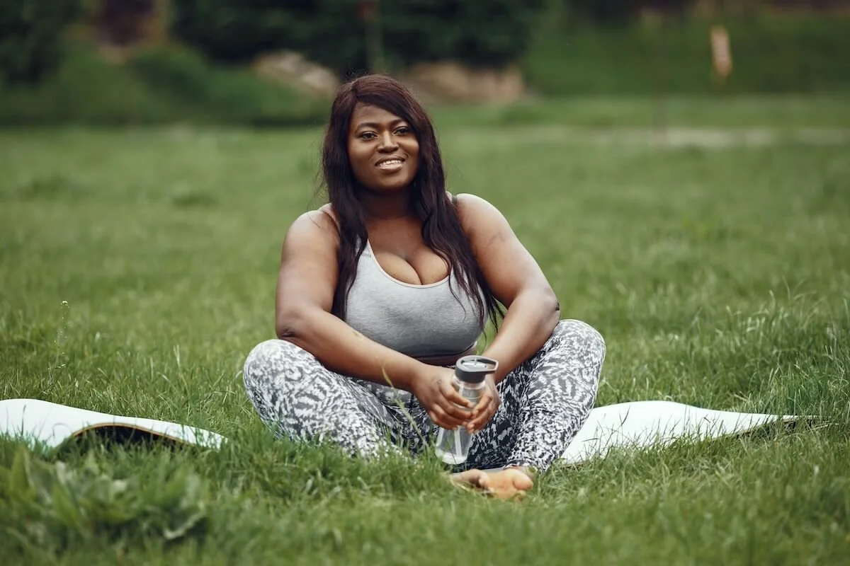 A woman sits confidently on a yoga mat outdoors holding a water bottle and smiling, reflecting the ease and self-acceptance that online eating disorder therapy in Utah can help you find beyond perfectionism in relationships.