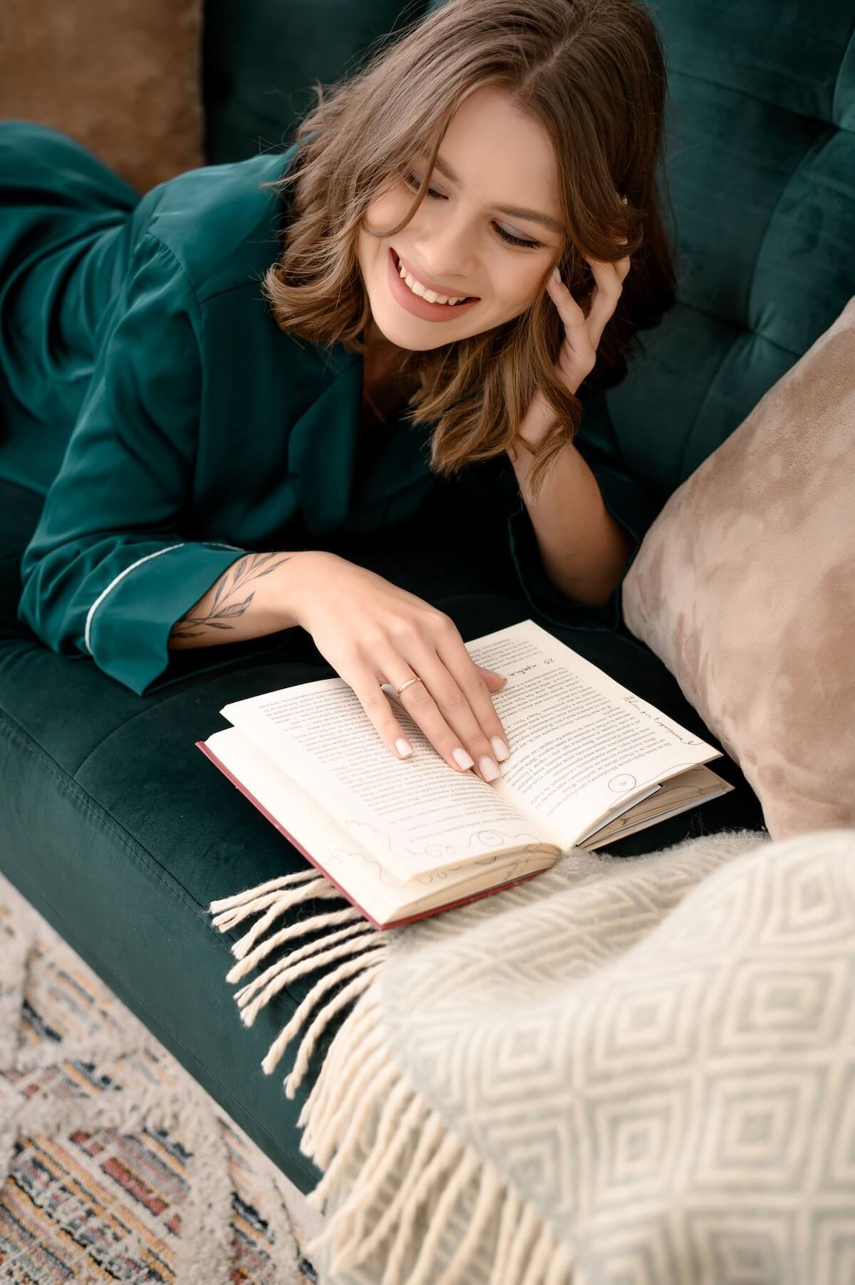 A woman smiles while reading on a couch, capturing the ease and presence that a body image therapist in Salt Lake City, UT and anxiety treatment in Salt Lake City can help you find your way back to.