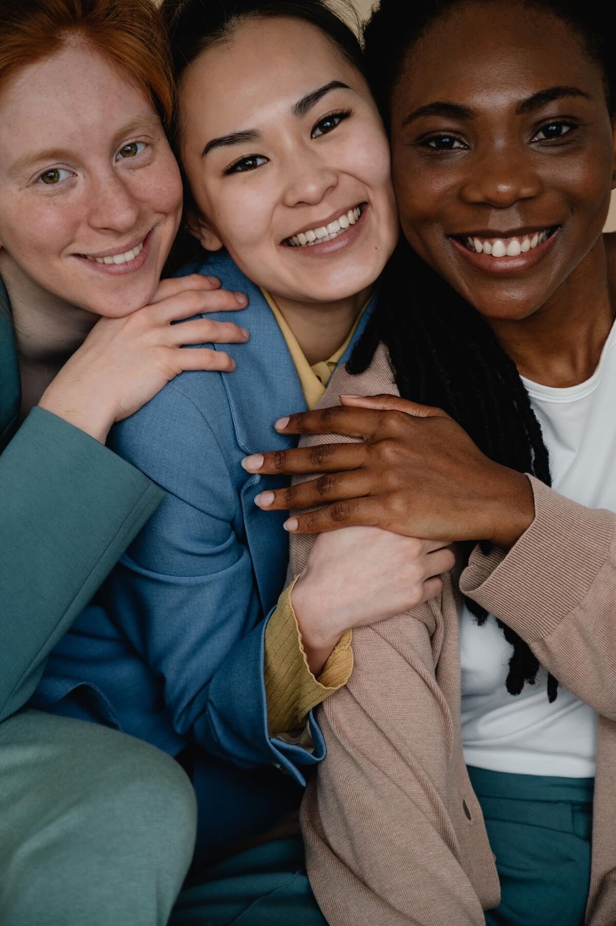 Three women of different backgrounds smile and embrace warmly, embodying the confidence and connection that body image counseling in Utah and a body image therapist in Provo, UT can help you work toward.