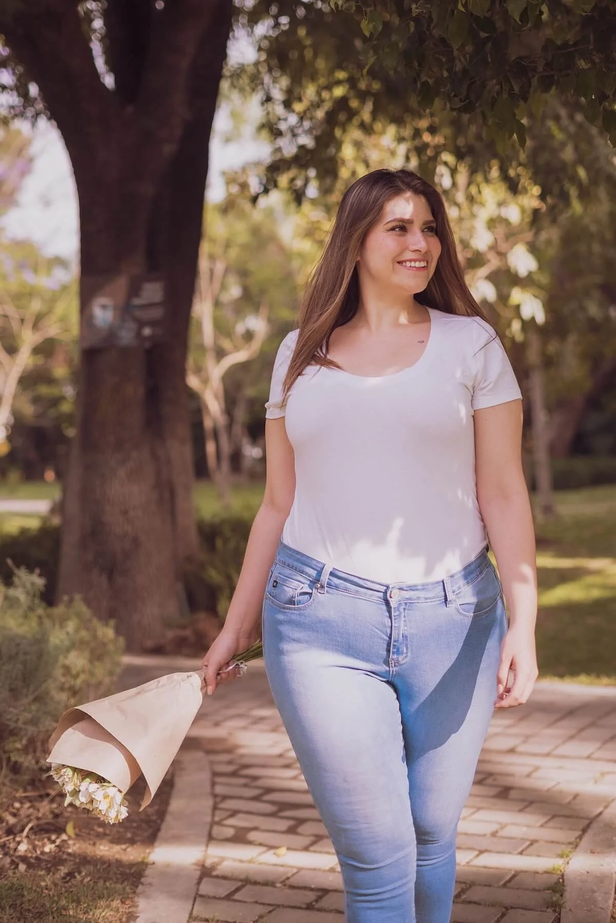 A woman walks confidently through a sunny park holding a bouquet of flowers, embodying the ease and freedom that eating disorder treatment in Utah and an eating disorder therapist in Provo can help you find your way back to.