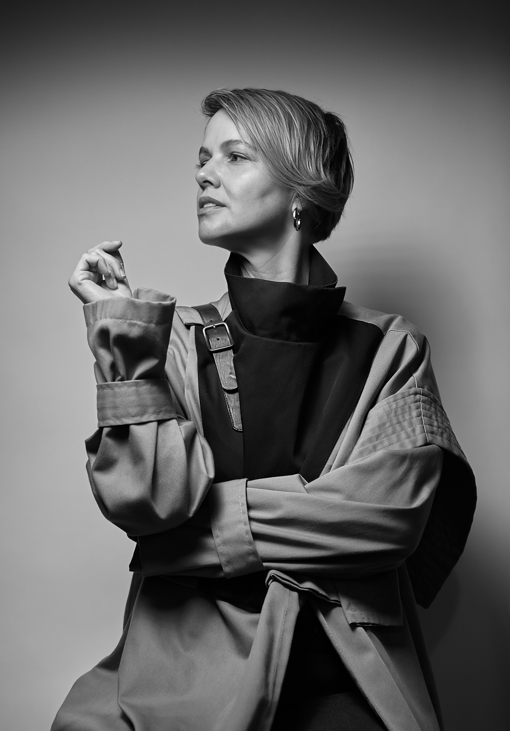 A black and white portrait of a woman with short hair, looking to the side with a confident expression, wearing a jacket with a high collar and a loose fit.
