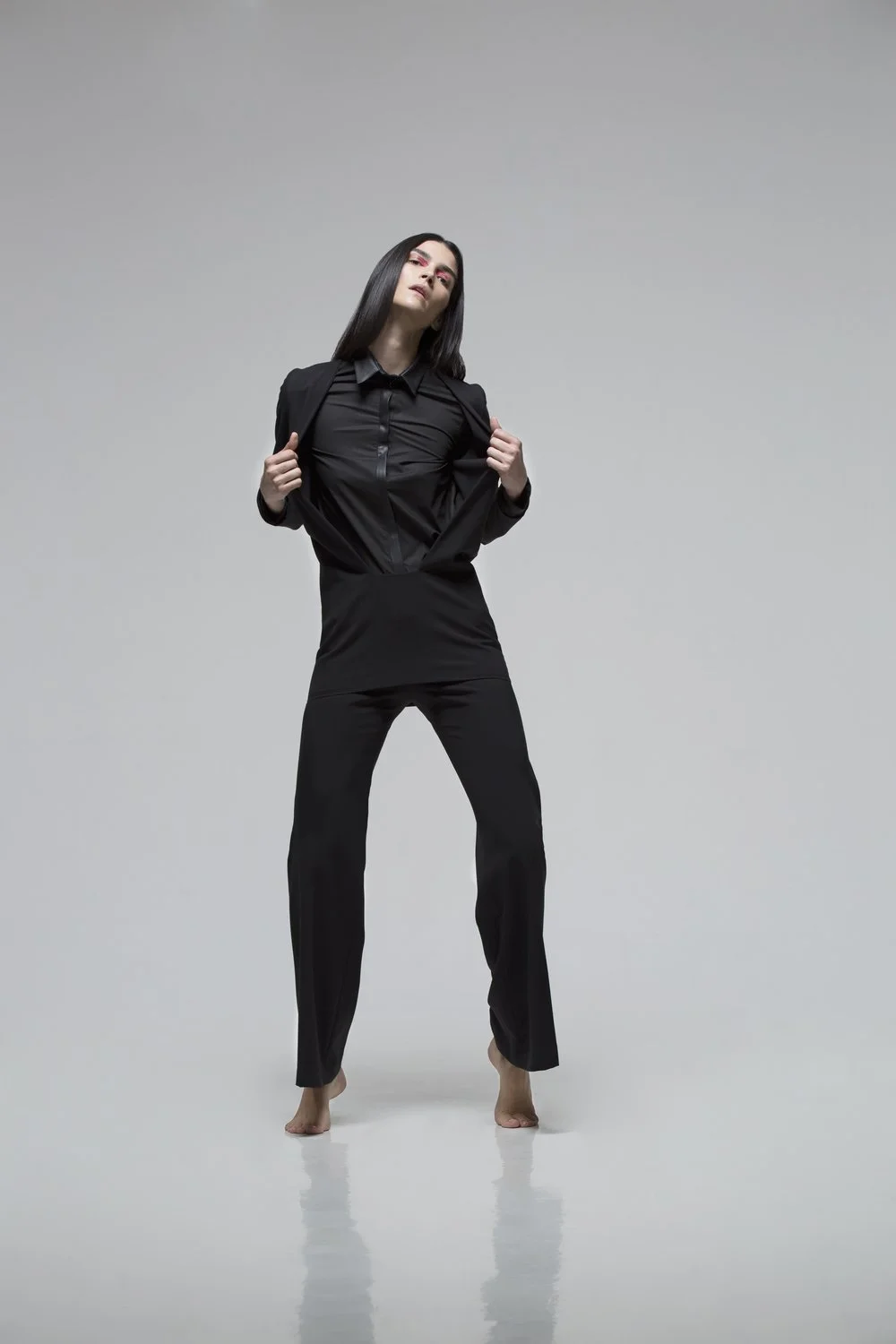 Woman standing barefoot in a black suit with a gray background.