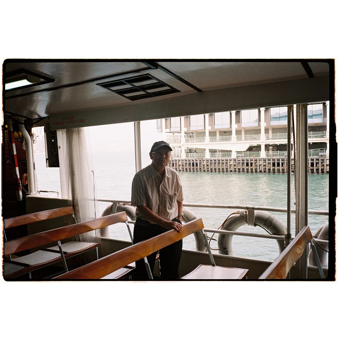 A man standing on a ferry boat with water and a pier visible outside the window.
