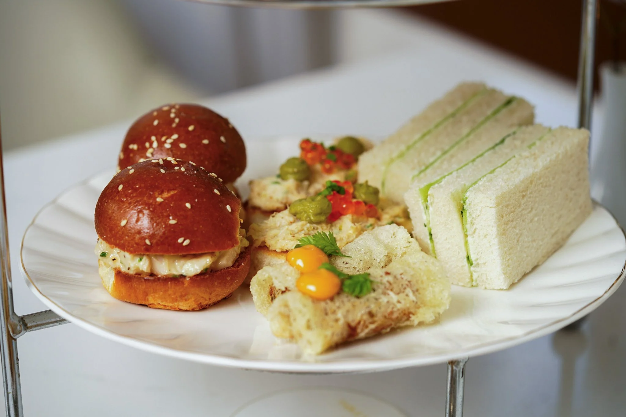 A plate with small sandwiches, mini burger buns with sesame seeds, on a tiered serving stand.