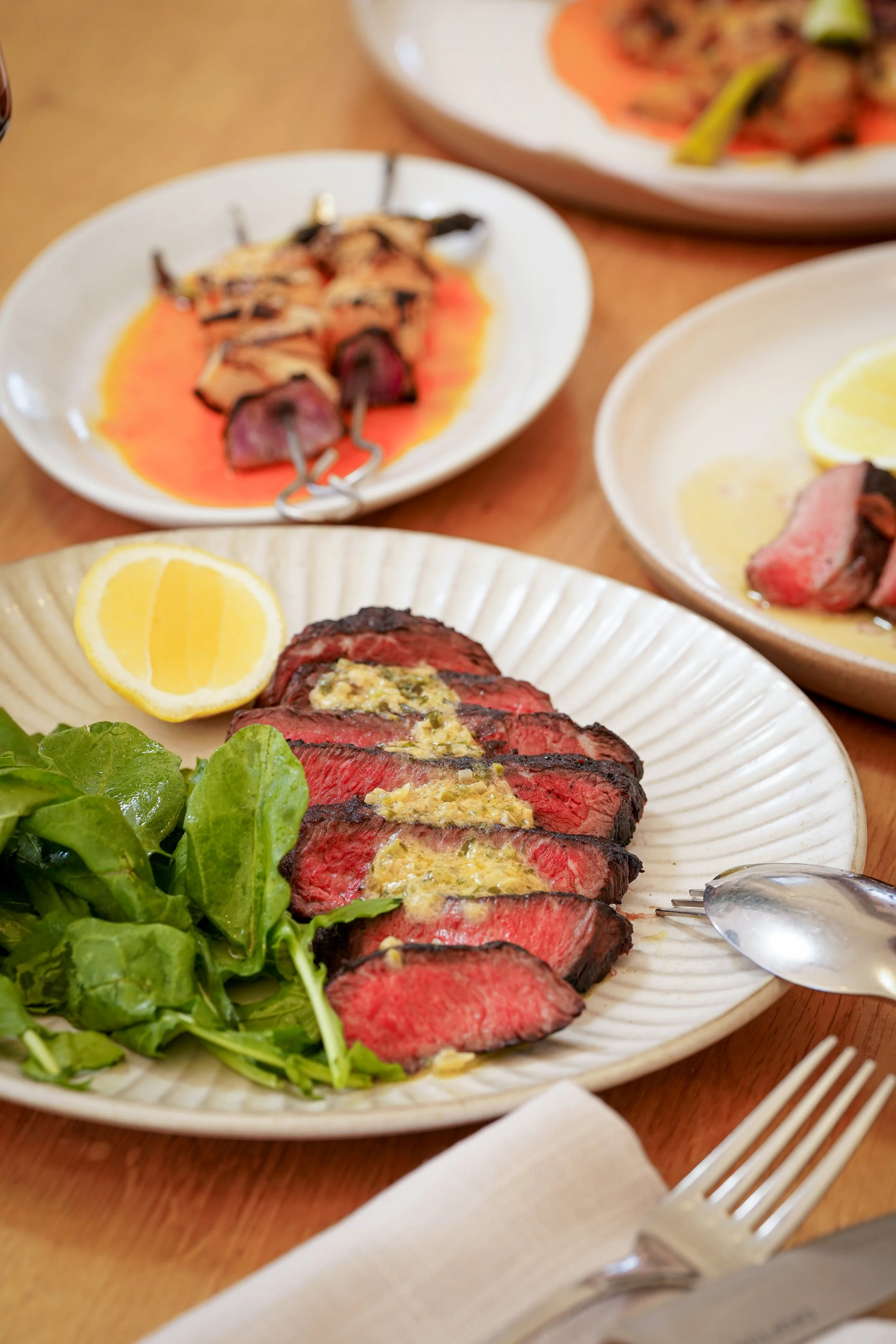 Sliced medium-rare steak with herb butter, served with fresh green salad and lemon wedge on a white plate, from a restaurant in Avalon.