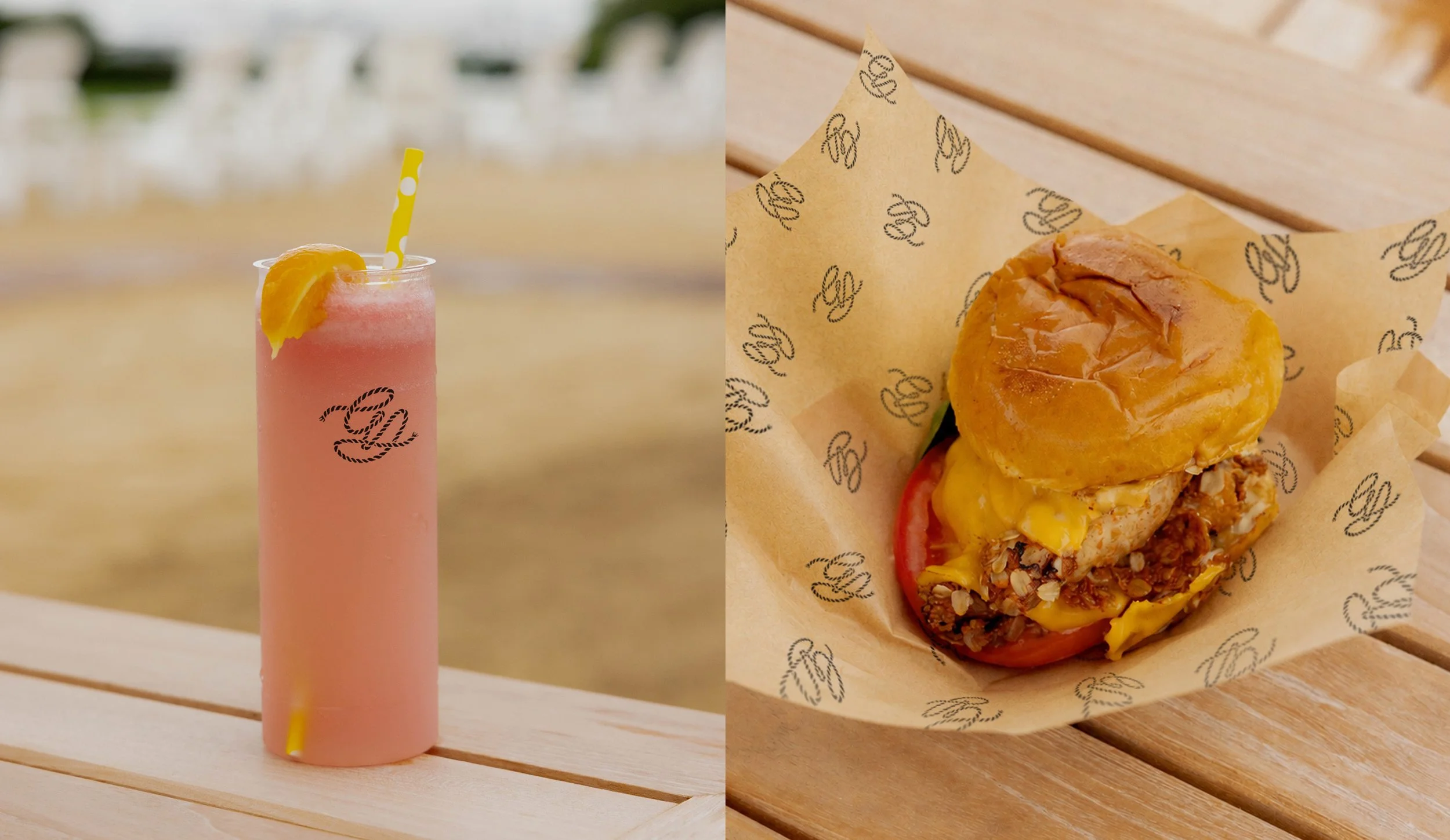 A pink frozen drink with a lemon wedge and a yellow polka-dot straw on a wooden table, and a cheeseburger with lettuce, tomato, cheese, and caramelized onions wrapped in branded paper.