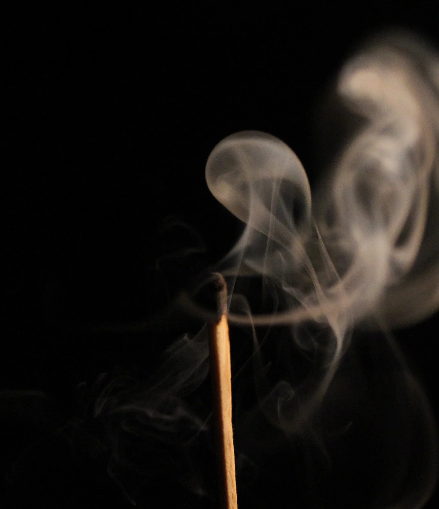 Close-up of a lit matchstick with smoke swirling upward against a black background.