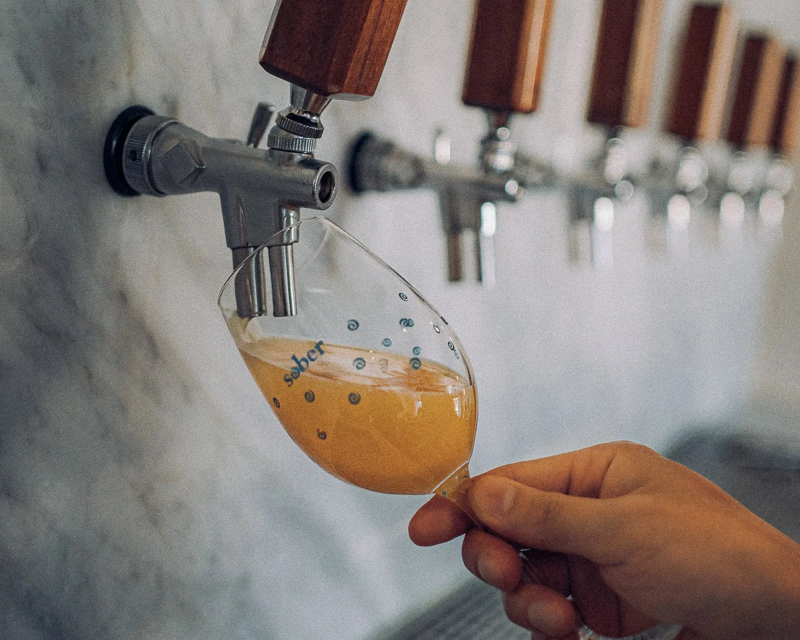 A person is pouring beer from a tap into a wine glass.