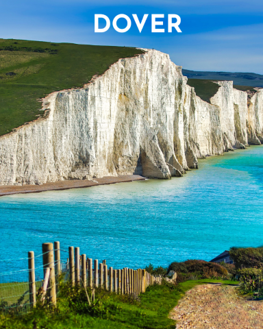 Chalk white cliffs capped in green over a calm turquoise sea.  A wood post fence lines the hill in the foreground.