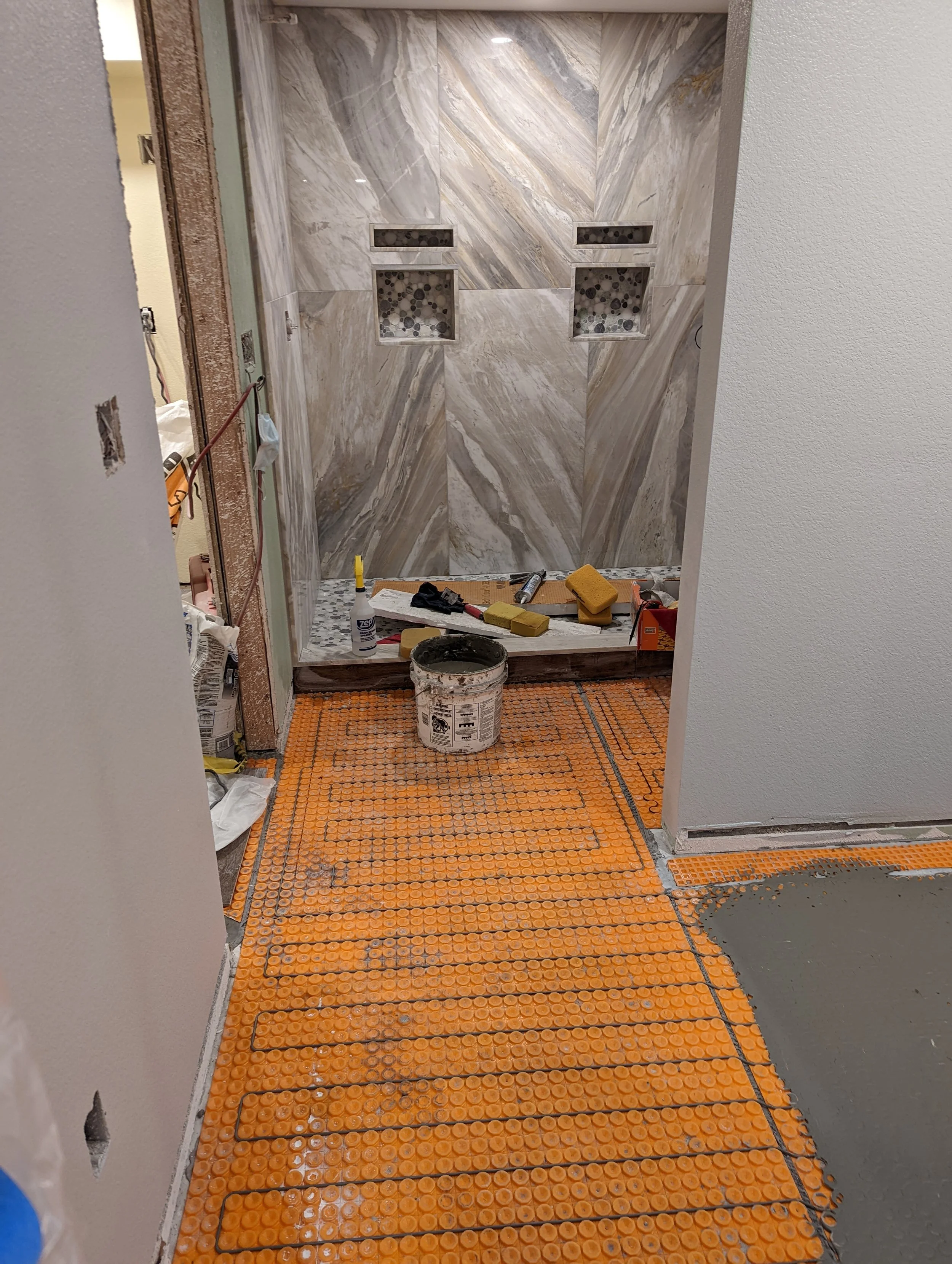 Shower pan and large format marble tile installed with ditra heat floor in Westminster, CO.  Shower has tiled niches and mosaic waterproofed pan with Denshield substrate for walls.