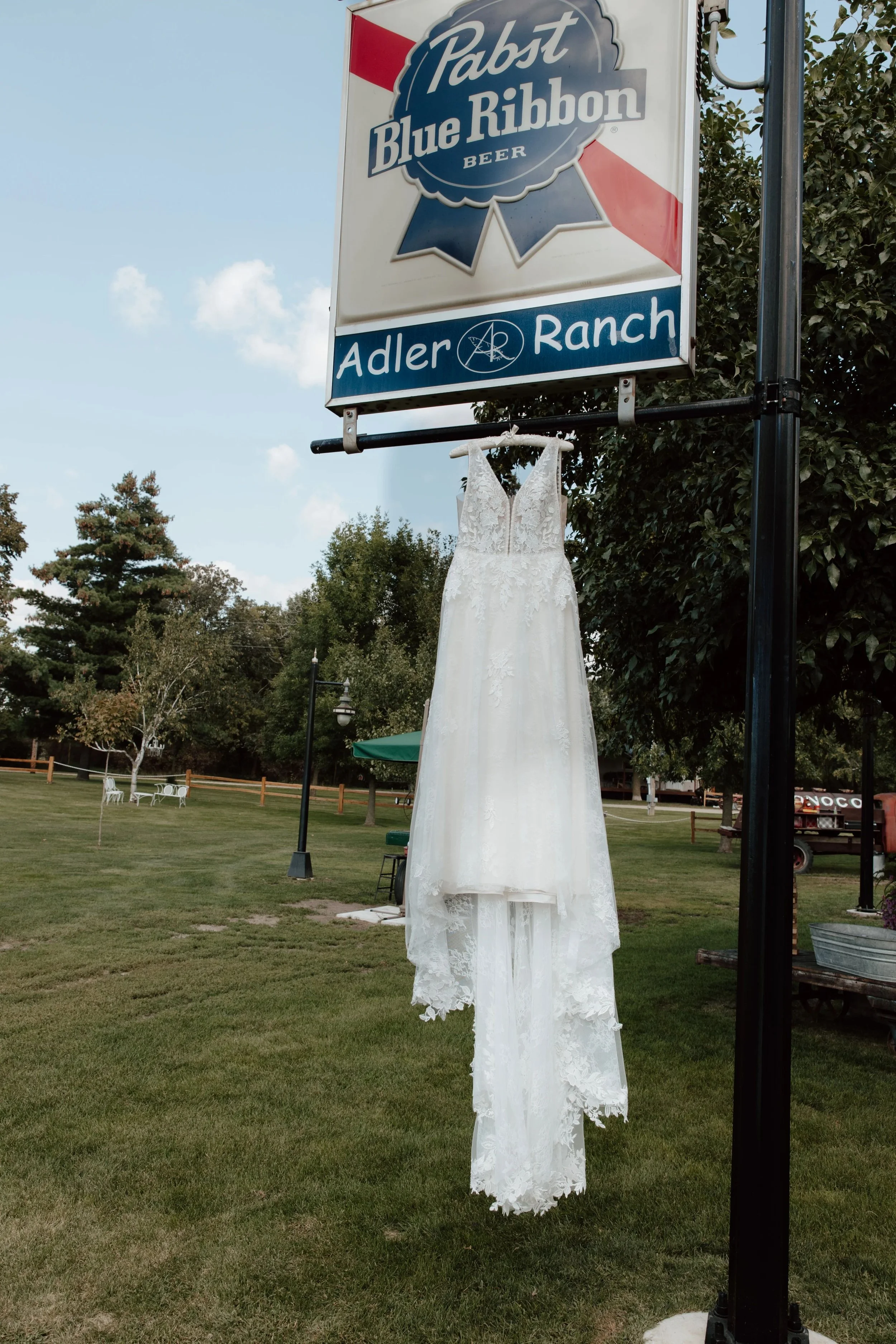 Photo of a wedding dress hung from the Adler Ranch Sign on a beautiful summer wedding day