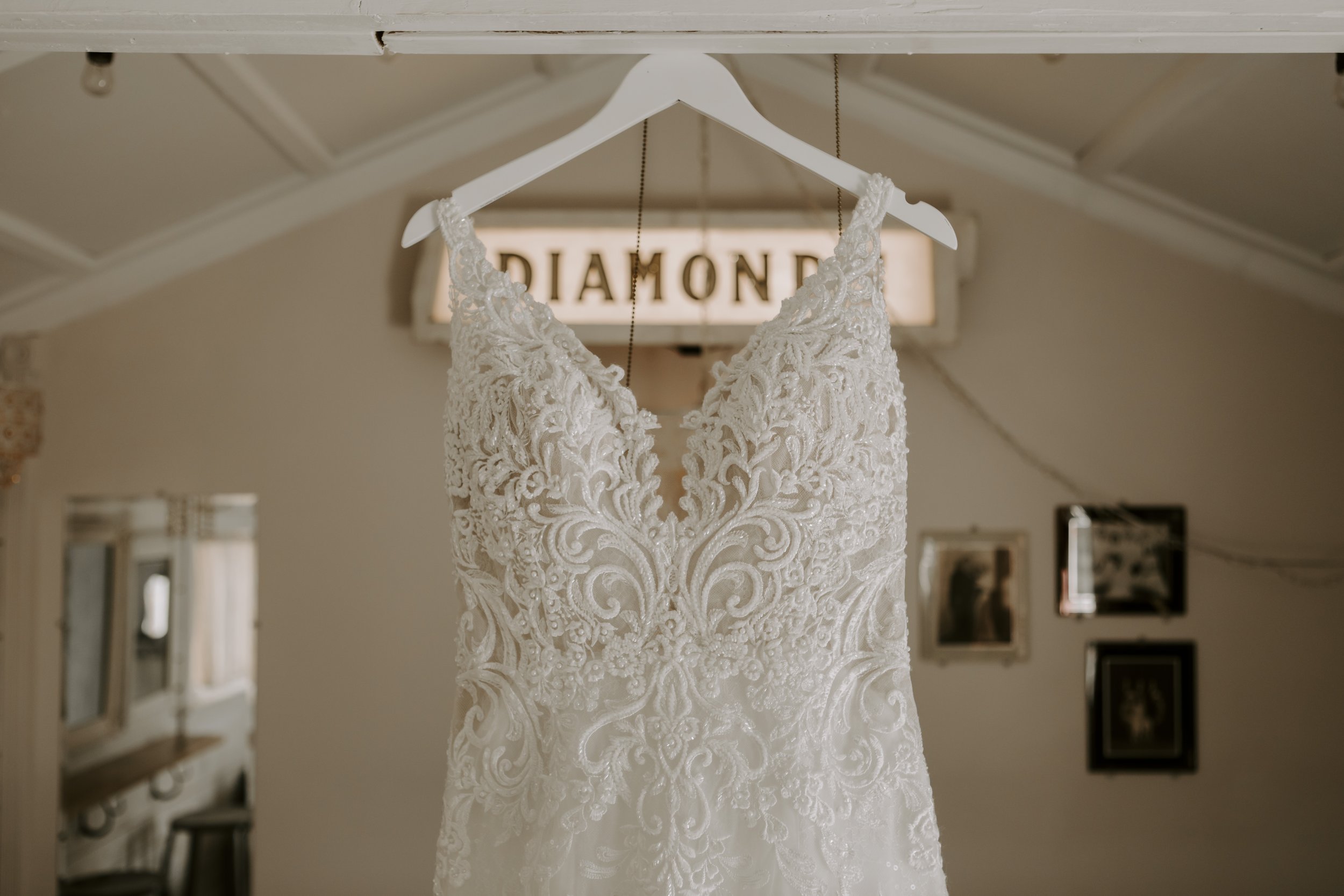 Photo of wedding dress hung up in The Cabin, a wedding party suite at MN Wedding Venue Adler Ranch with vintage Diamond sign in background. What to do with leftover wedding dress material