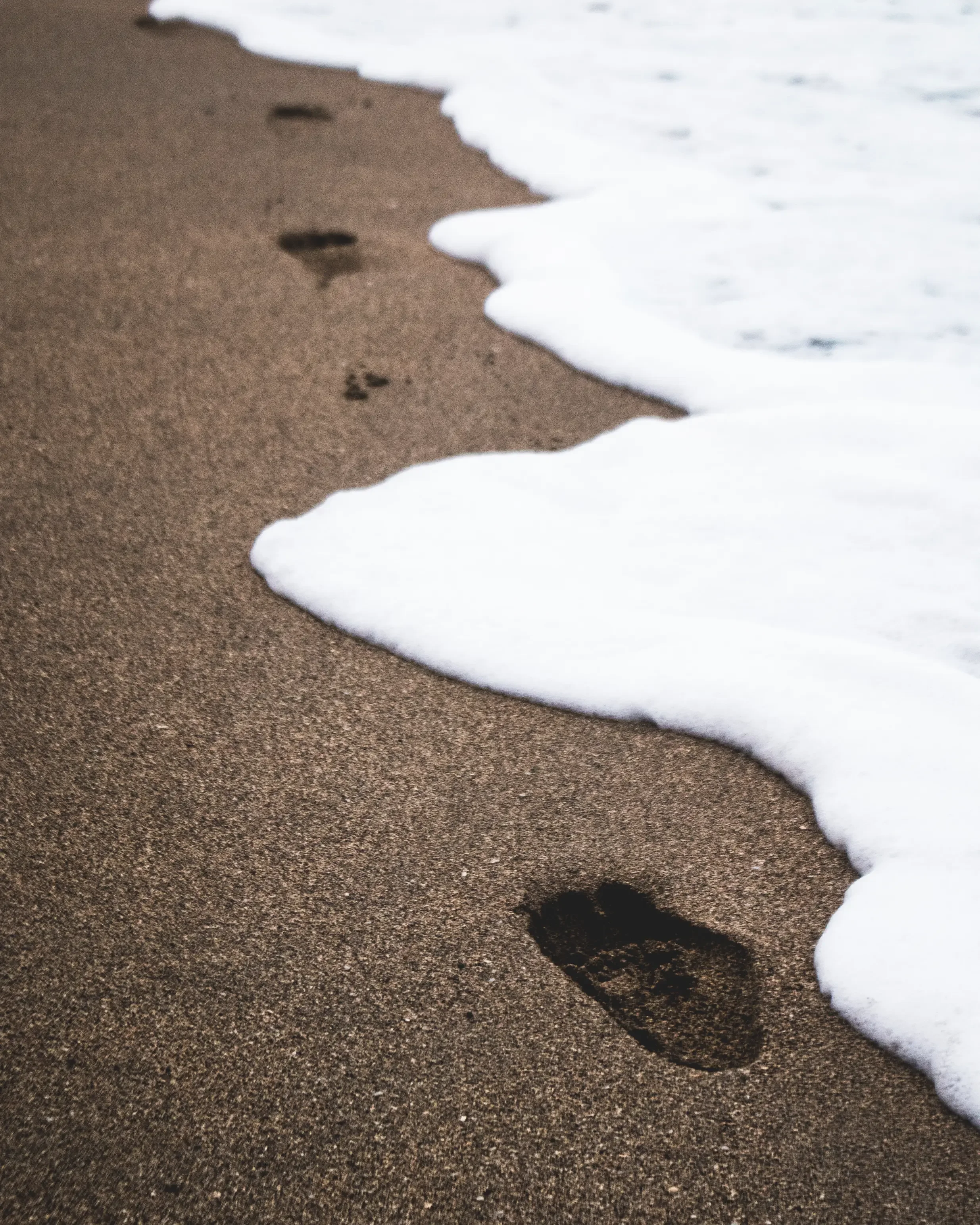Phil Williams' footprints in wet sand as sea foam washes in at Playa Cocles, Puerto Viejo, Costa Rica