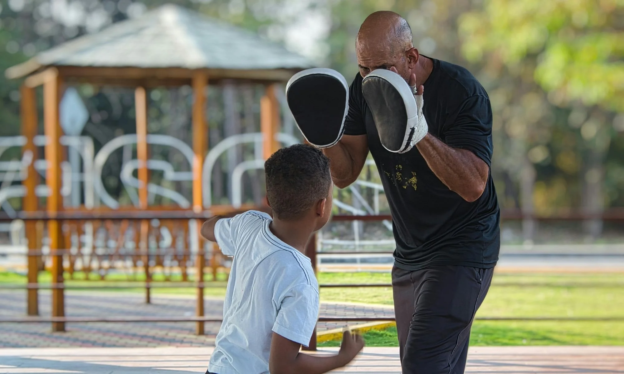 Father practicing boxing in a park with son.