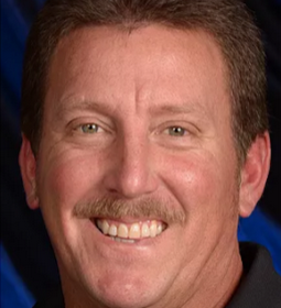 Close-up of smiling man with short brown hair and mustache, wearing a dark shirt.