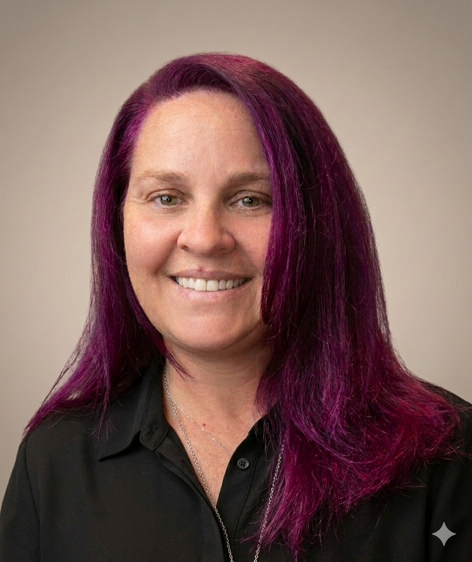 A woman with purple hair smiling in front of a plain light-colored background.