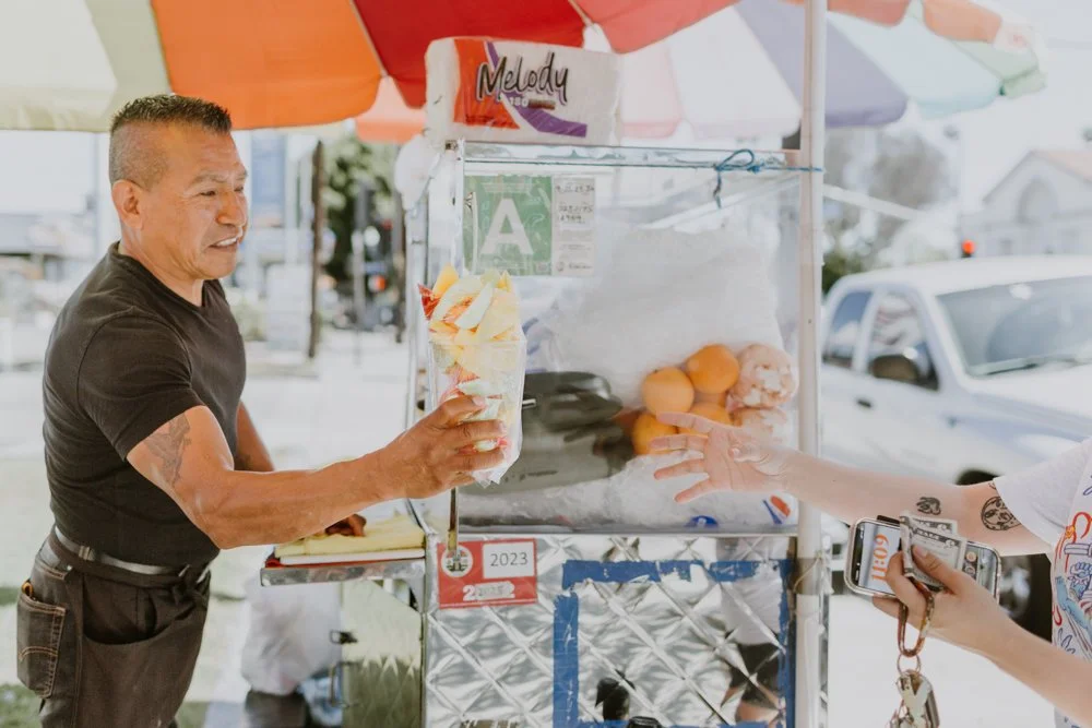 Local street vendor handing fruit to a customer at a cart in Northeast Los Angeles