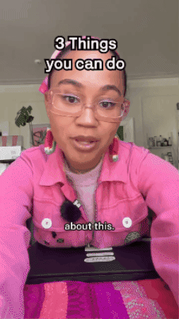 Woman with glasses and pink shirt speaking in a room with plants and shelves in the background.