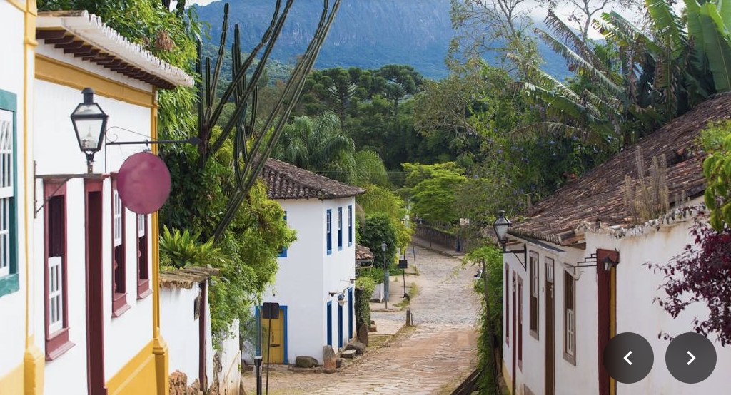 A picturesque cobblestone street in a colorful, lush village with mountains in the background.