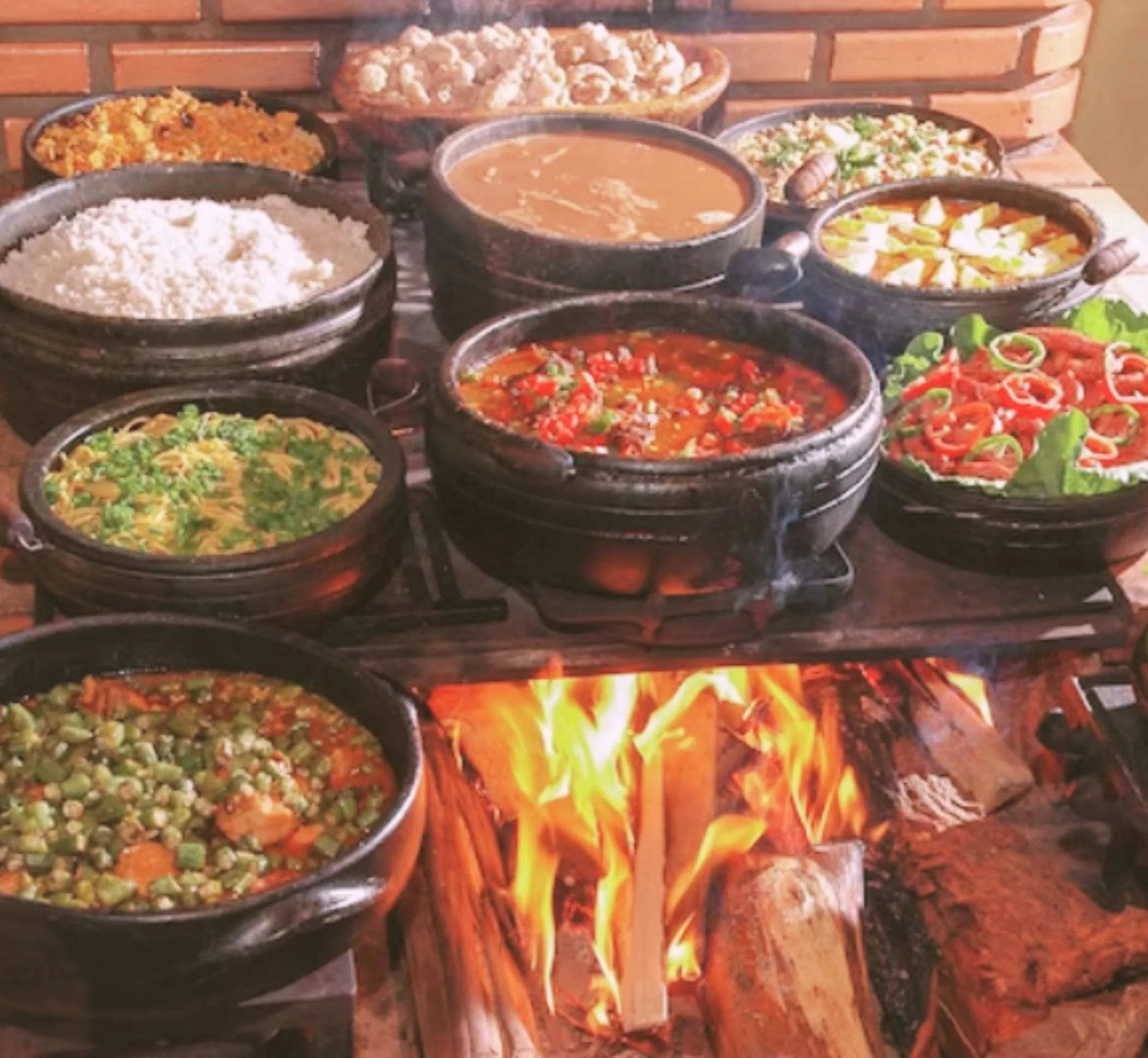 Assorted Mexican dishes cooking on a traditional outdoor grill with flames and wood underneath