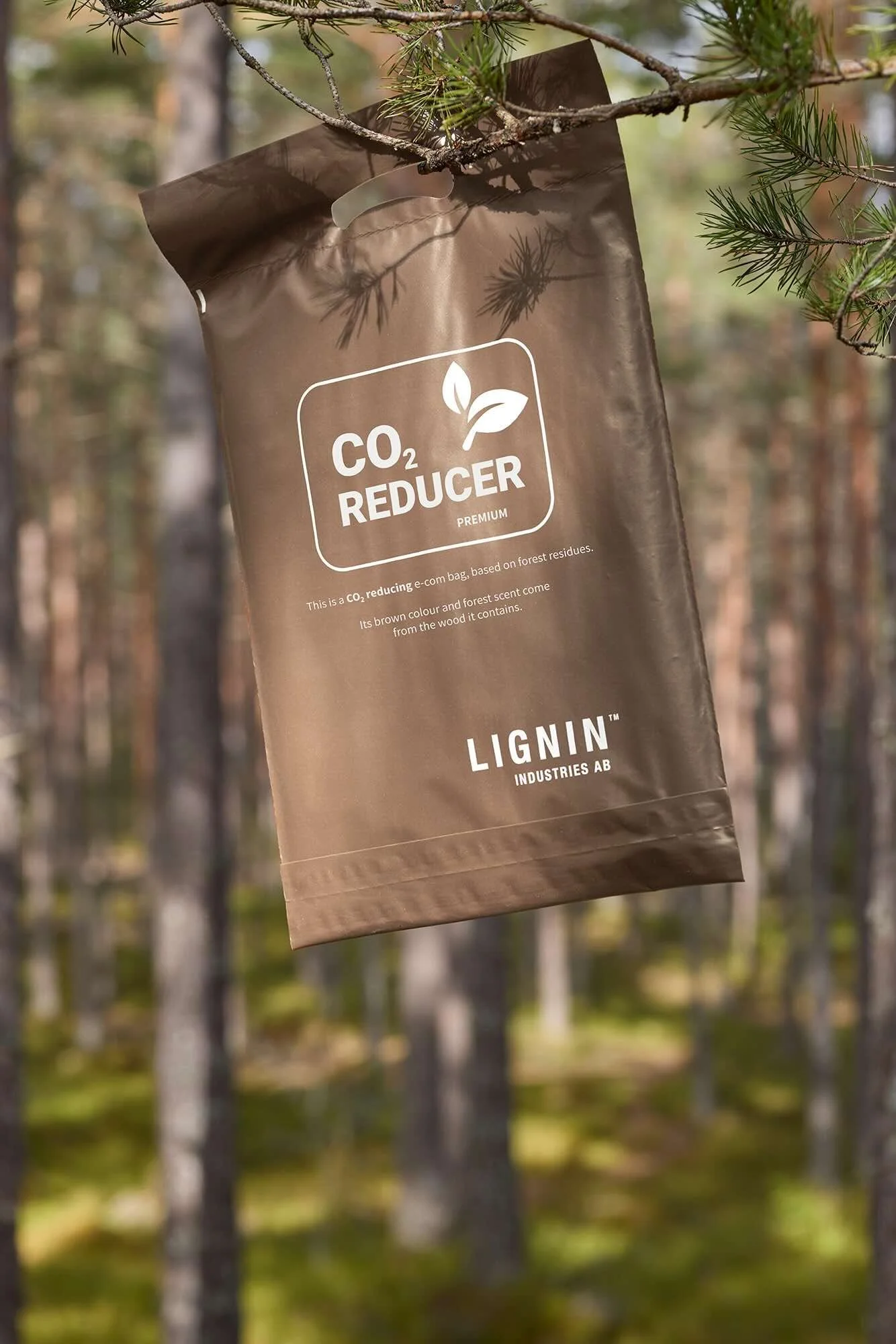 Sustainable brown e-commerce bag made from polyethylene film containing Renol, hanging from a branch with a forest in the background. CO₂-reduced. Lignin Industries.