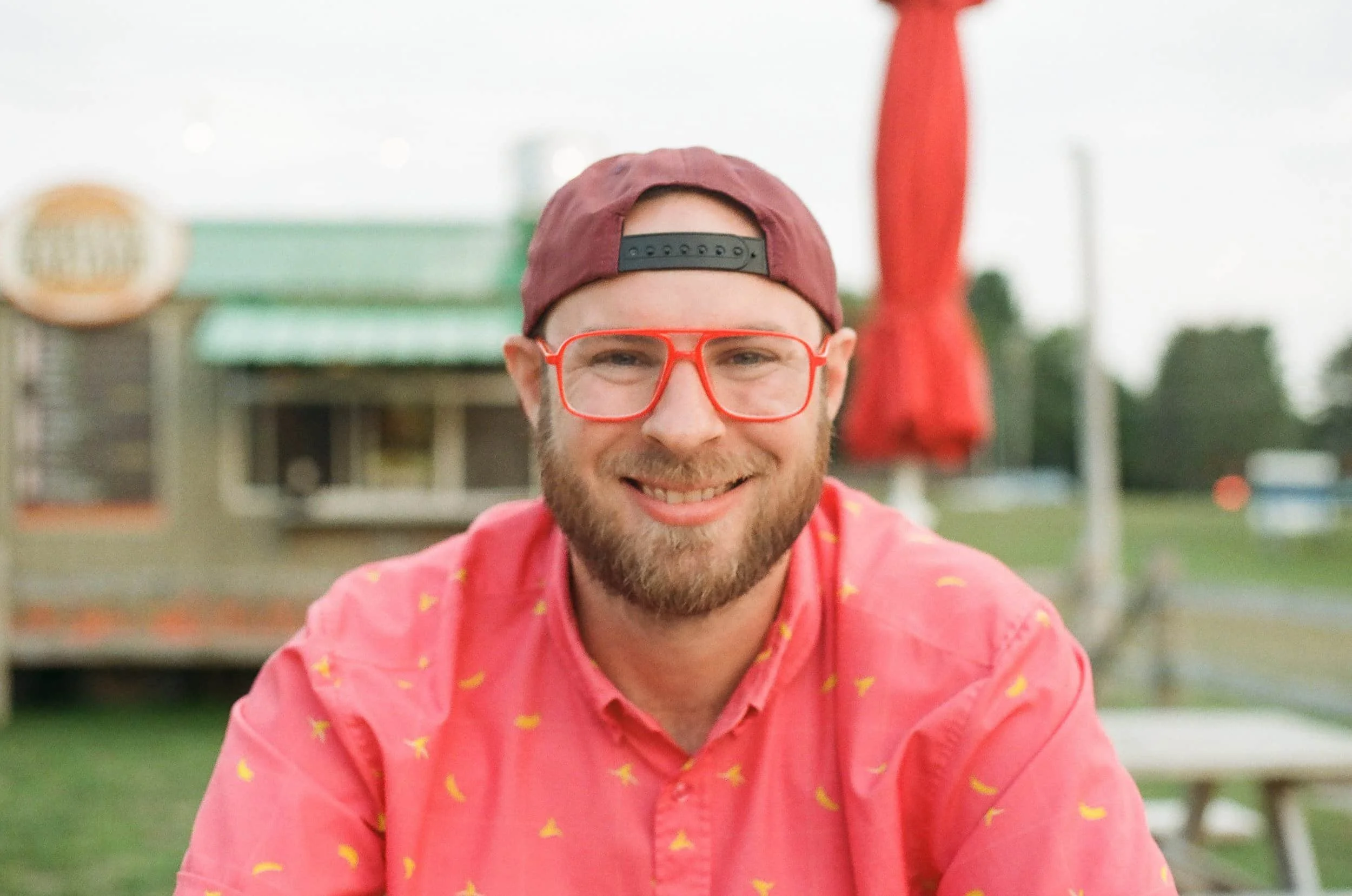 man with glasses, beard, and backwards hat sitting in front of a food truck