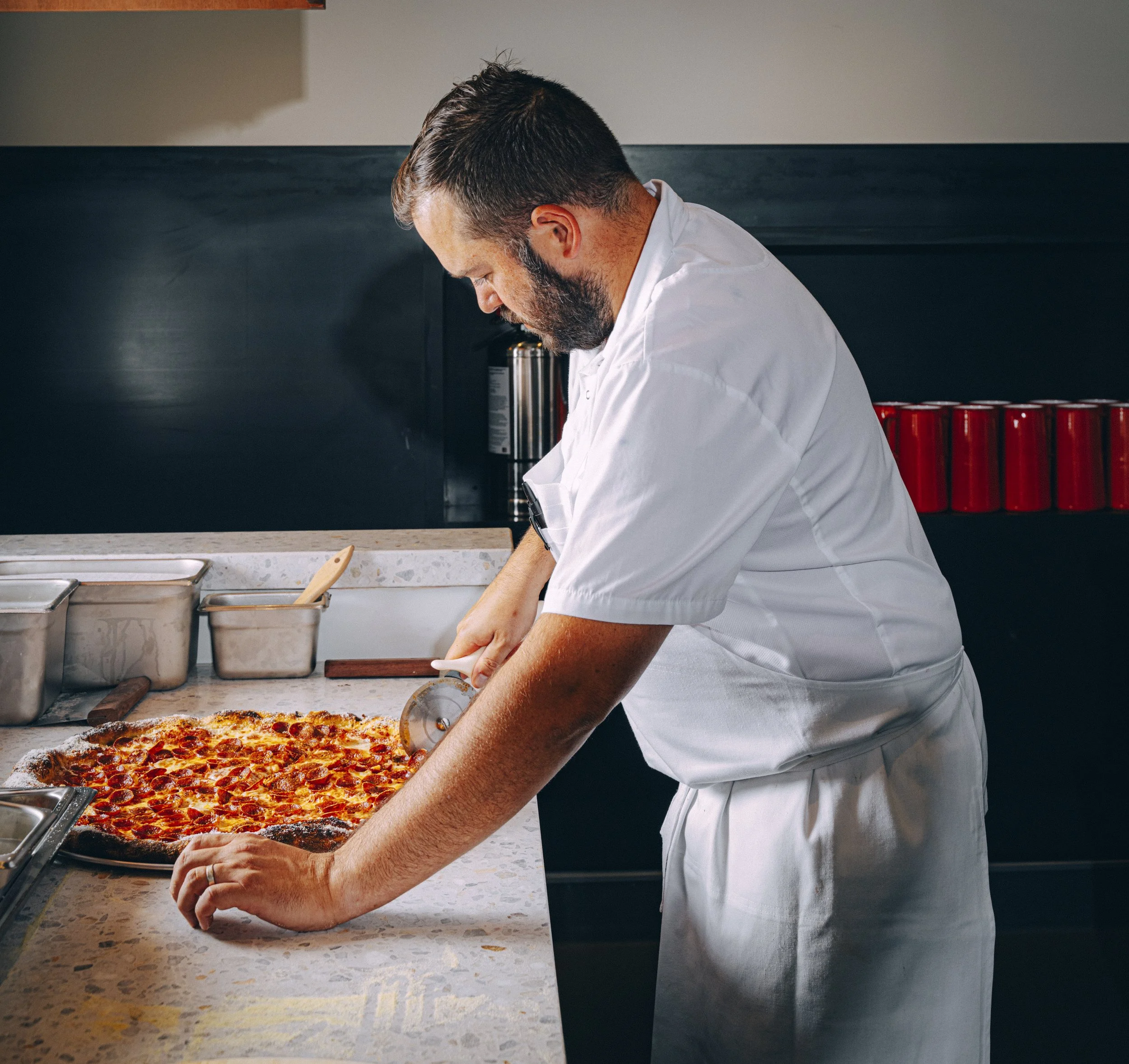 Chef slicing a freshly baked pepperoni pizza in a kitchen.