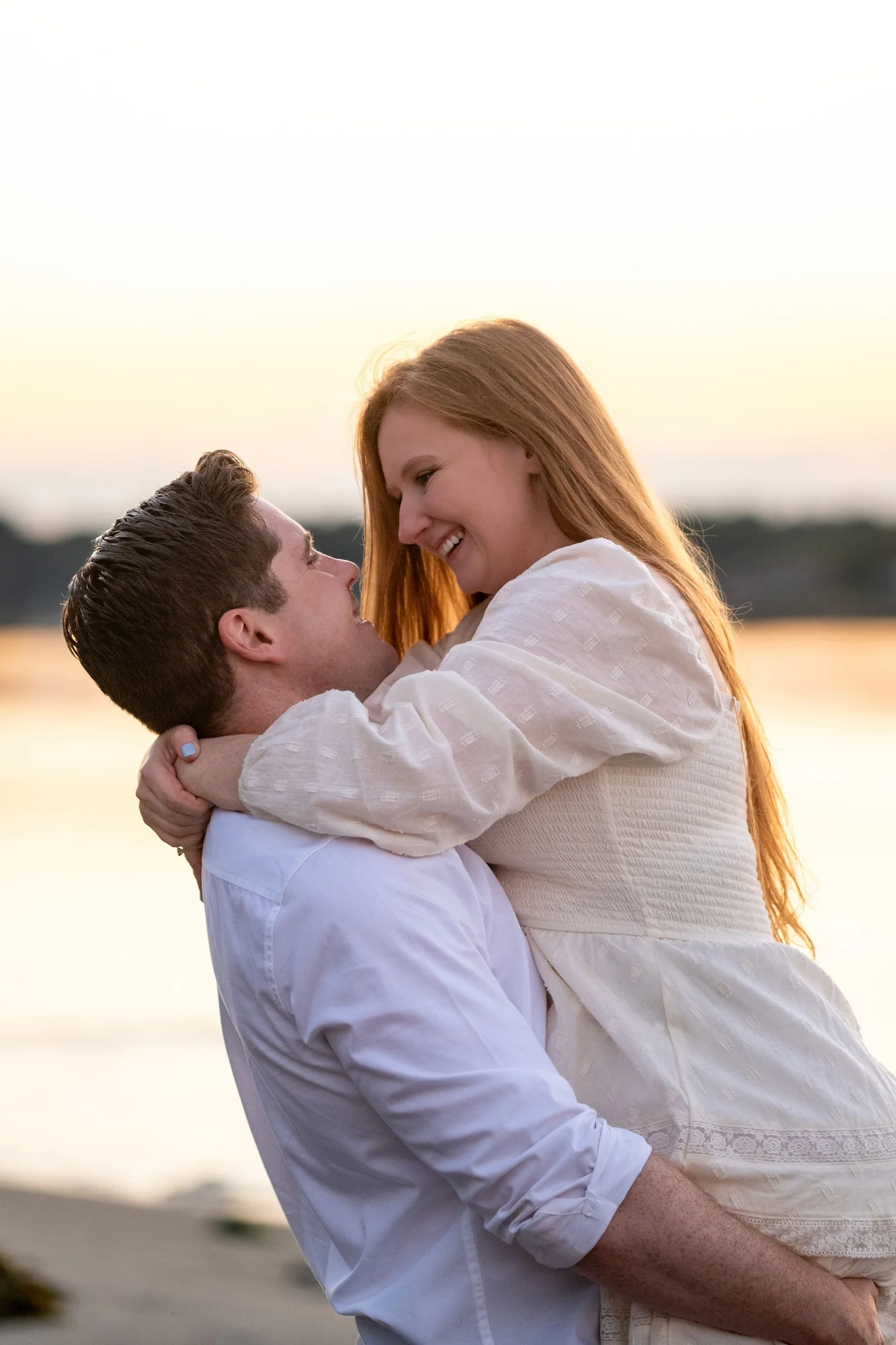 Kayla and Ethan engaged couple lift embrace backlit sunset coastal Odiorne Point State Park New Hampshire engagement photography VMG Productions