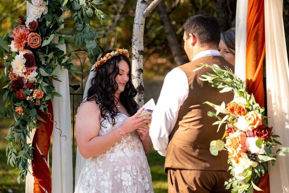 Meagan and Joshua kissing under floral arch at The Watson Homestead Hiram Maine fall wedding photography VMG Productions