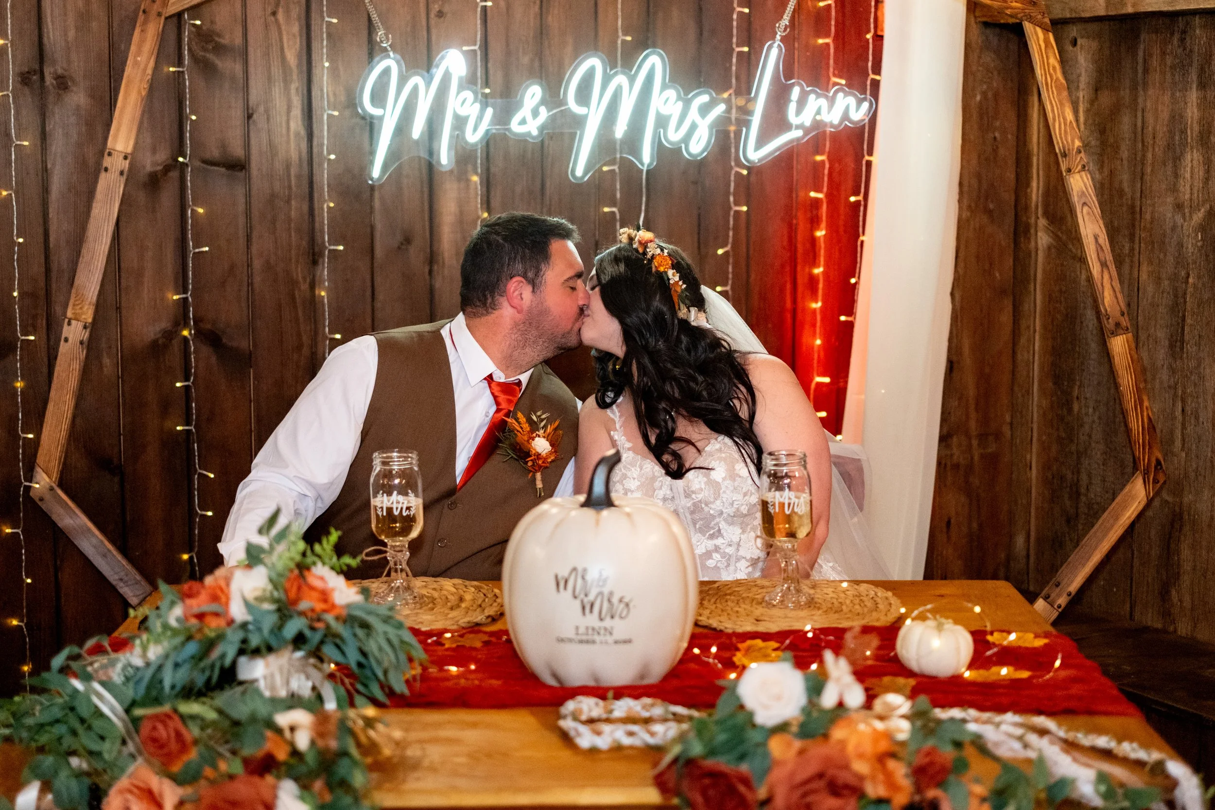 Meagan and Joshua kissing at sweetheart table in barn reception at The Watson Homestead Hiram Maine fall wedding photography VMG Productions