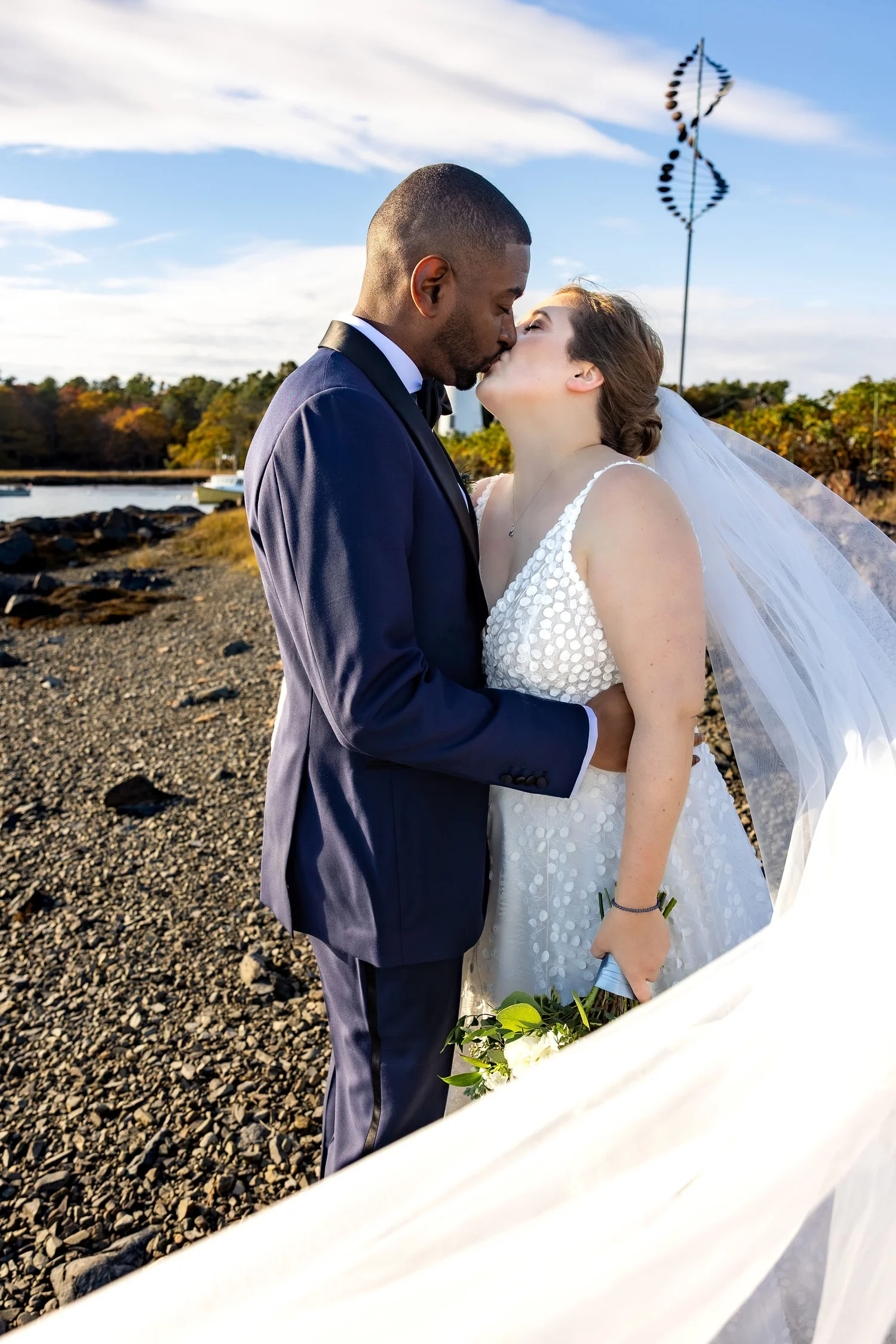 Kaitlyn and Darren kissing with lighthouse backdrop coastal Kennebunkport Maine fall wedding portrait VMG Productions