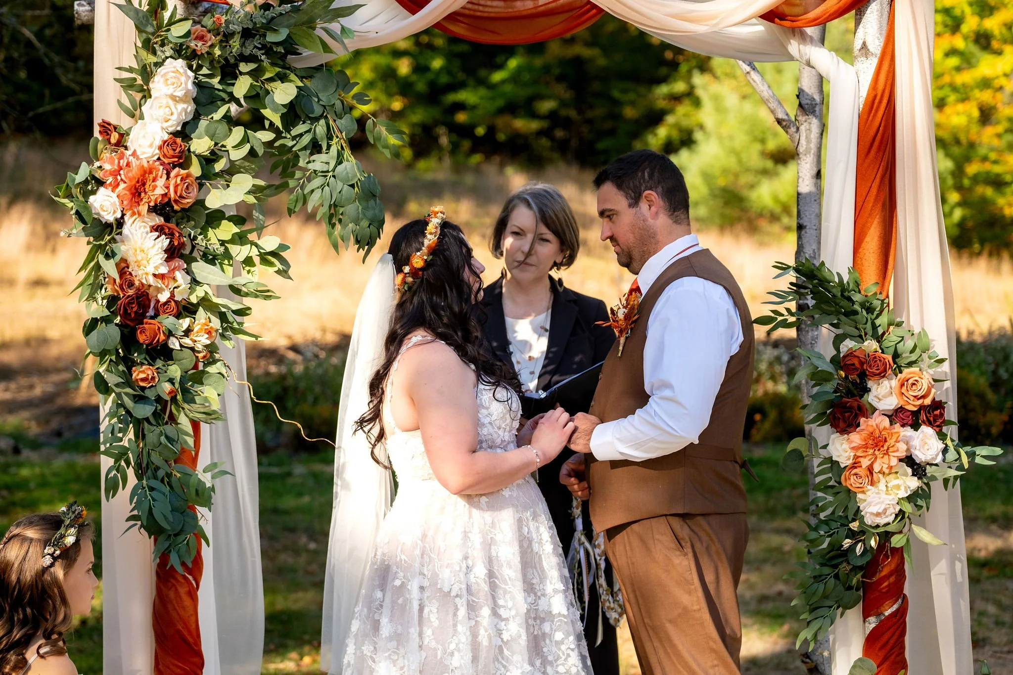 Meagan and Joshua exchanging vows under floral arch at The Watson Homestead Hiram Maine fall wedding photography VMG Productions