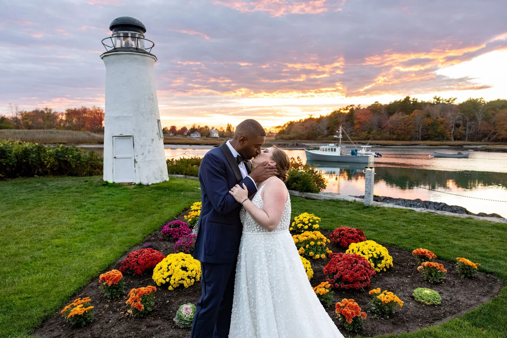 Kaitlyn and Darren kissing in front of lighthouse with fall flower beds at sunset Nonantum Resort Kennebunkport Maine wedding VMG Productions