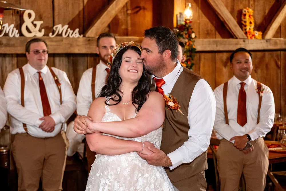 Joshua kissing Meagan during reception in rustic barn at The Watson Homestead Hiram Maine fall wedding photography VMG Productions