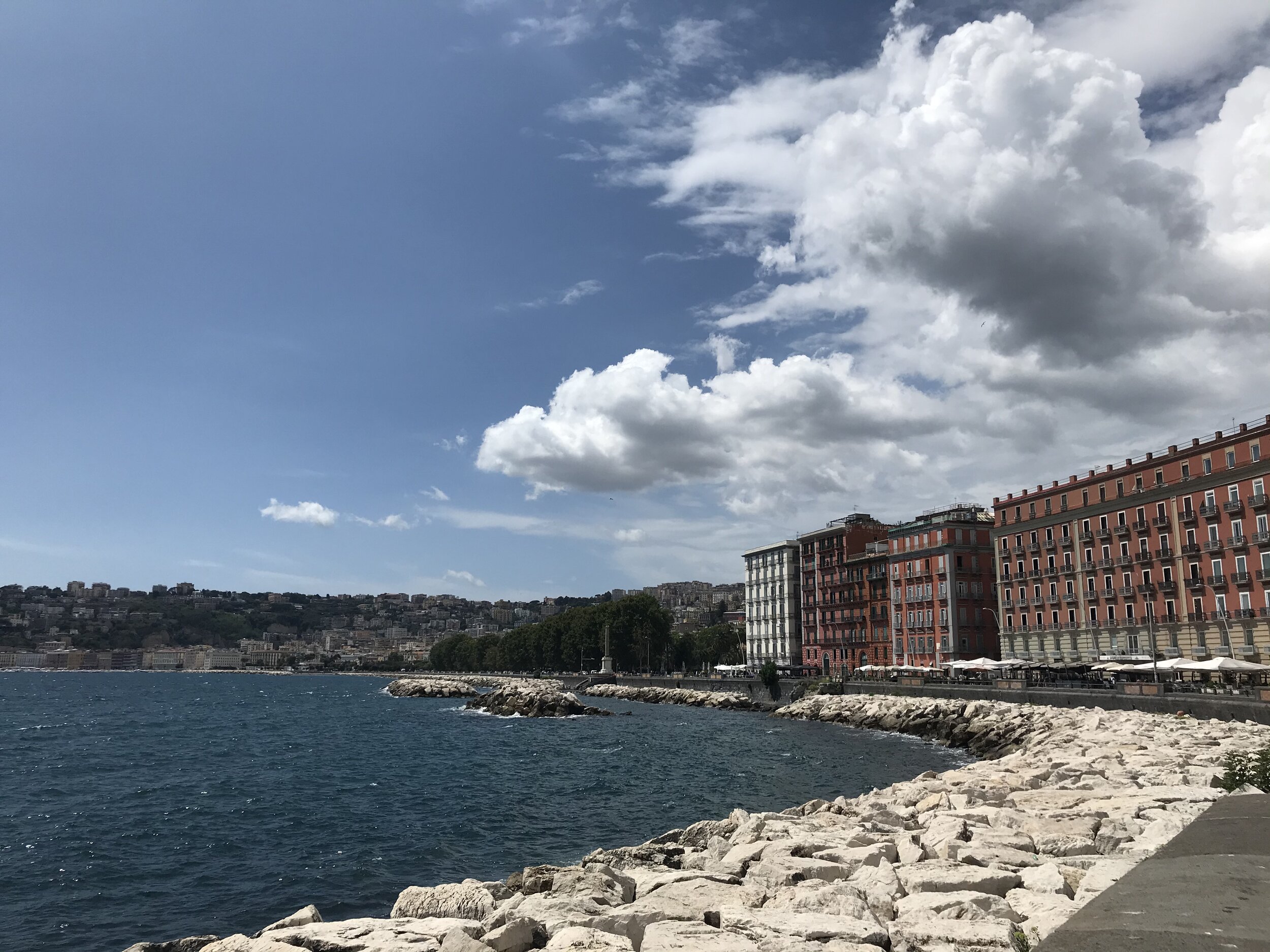 NAPOLI, Italy. August 7th, 2020. PICTURED: The Lungo Mare or “long sea road” stretches around the corner on which sits Castel Dell’ovo. Restaurants, hotels, and diving rocks sit on the sunny Mediterranean.