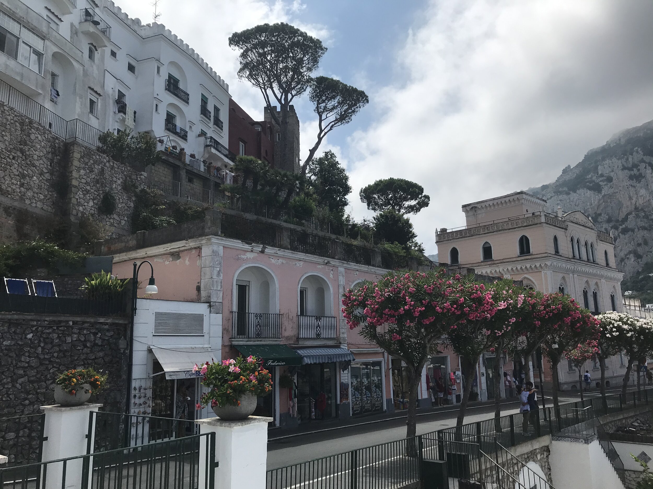  CAPRI, Napoli. August 4th, 2020. PICTURED: Shops fill the rose-colored arcade in the town center of Capri as clouds briefly roll in to give respite from the blazing sun. 